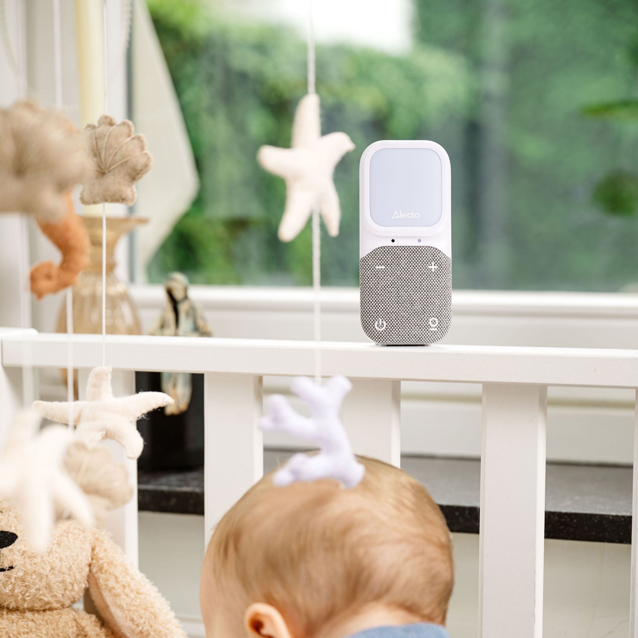 Ein Babyphone steht auf einem weißen Gitterbett, daneben Spielzeug.