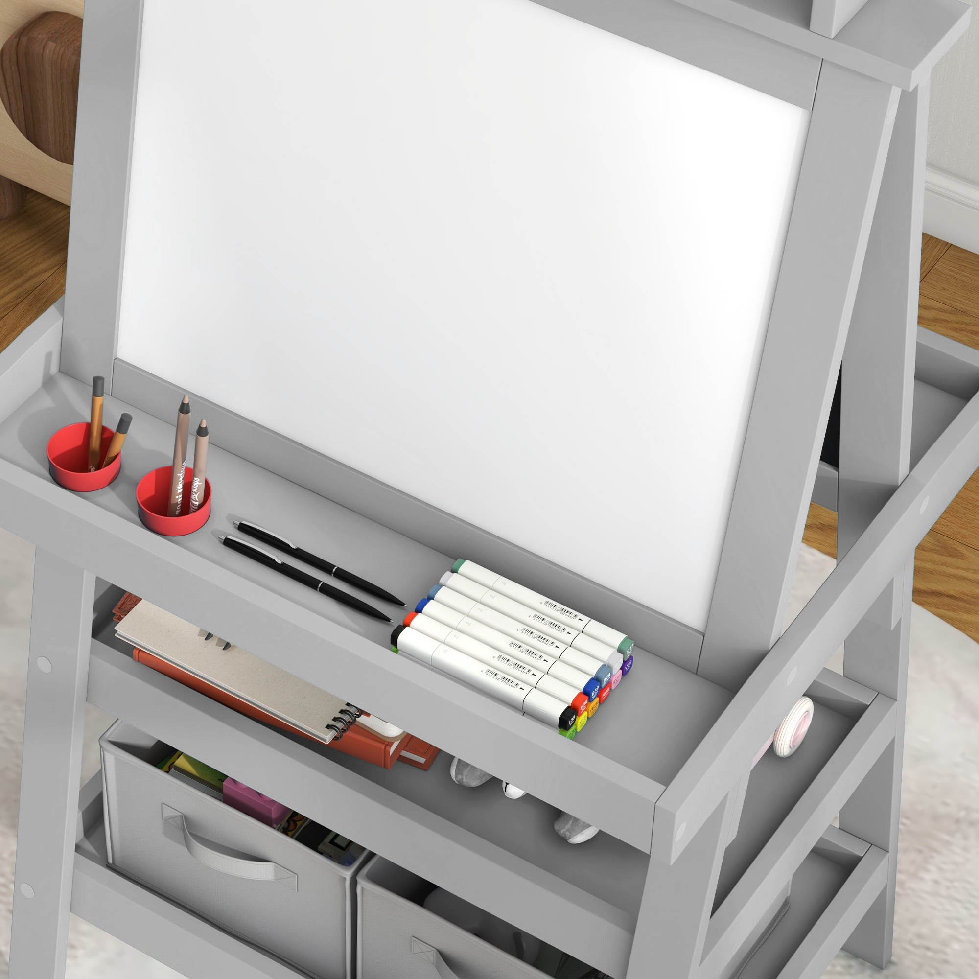 Un caballete infantil gris con pizarra blanca, bolígrafos, libros y cajas de almacenaje.