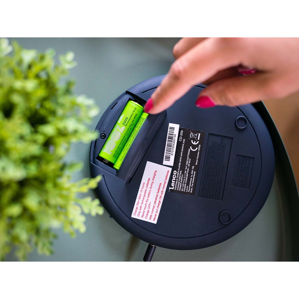 Ręka wkłada zieloną baterię AA do czarnego urządzenia.