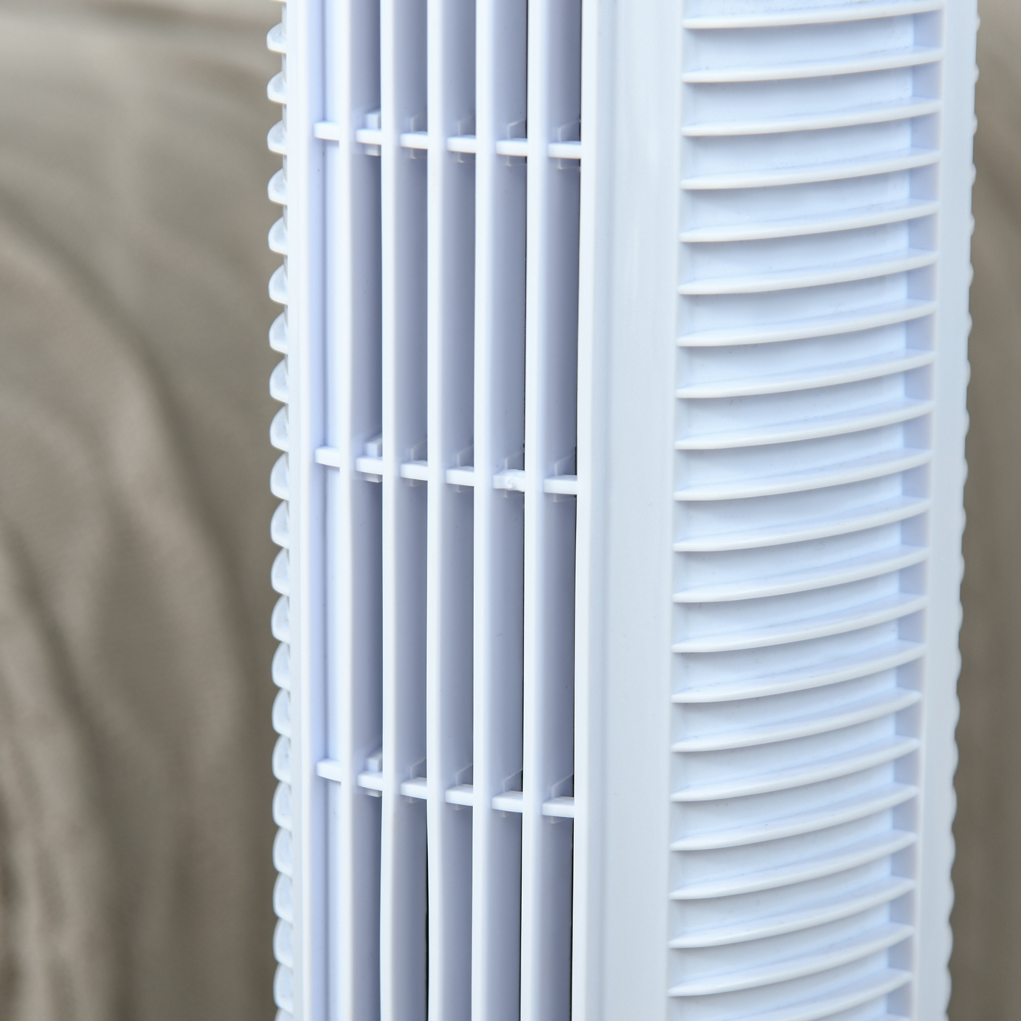 Primer plano de un ventilador vertical blanco con rejillas y celosía. Fondo desenfocado.