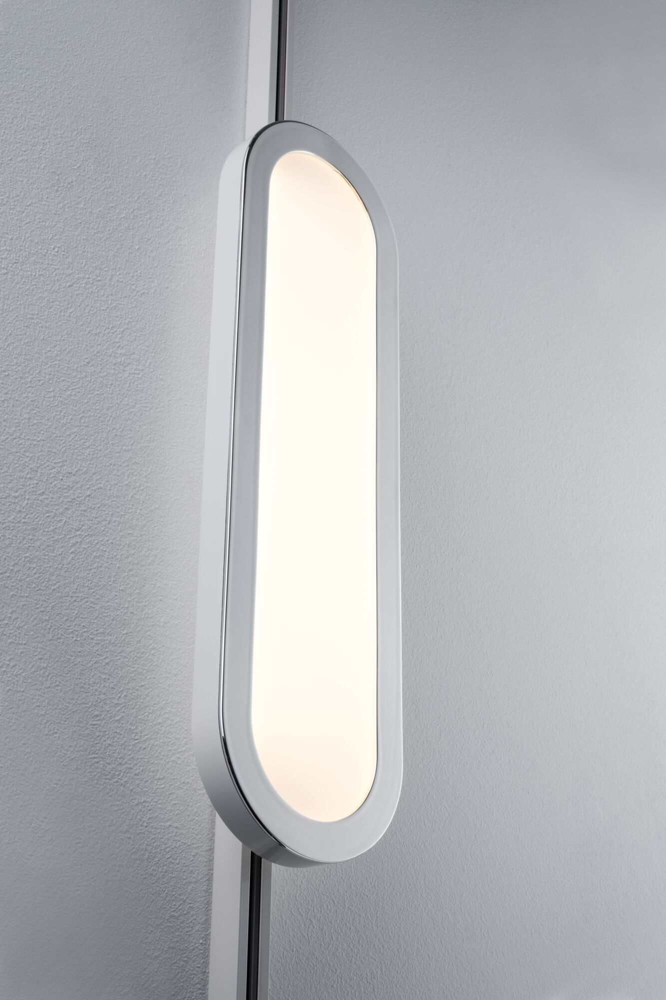 Un apparecchio ovale verticale con cornice bianca e bordo cromato su un muro grigio.