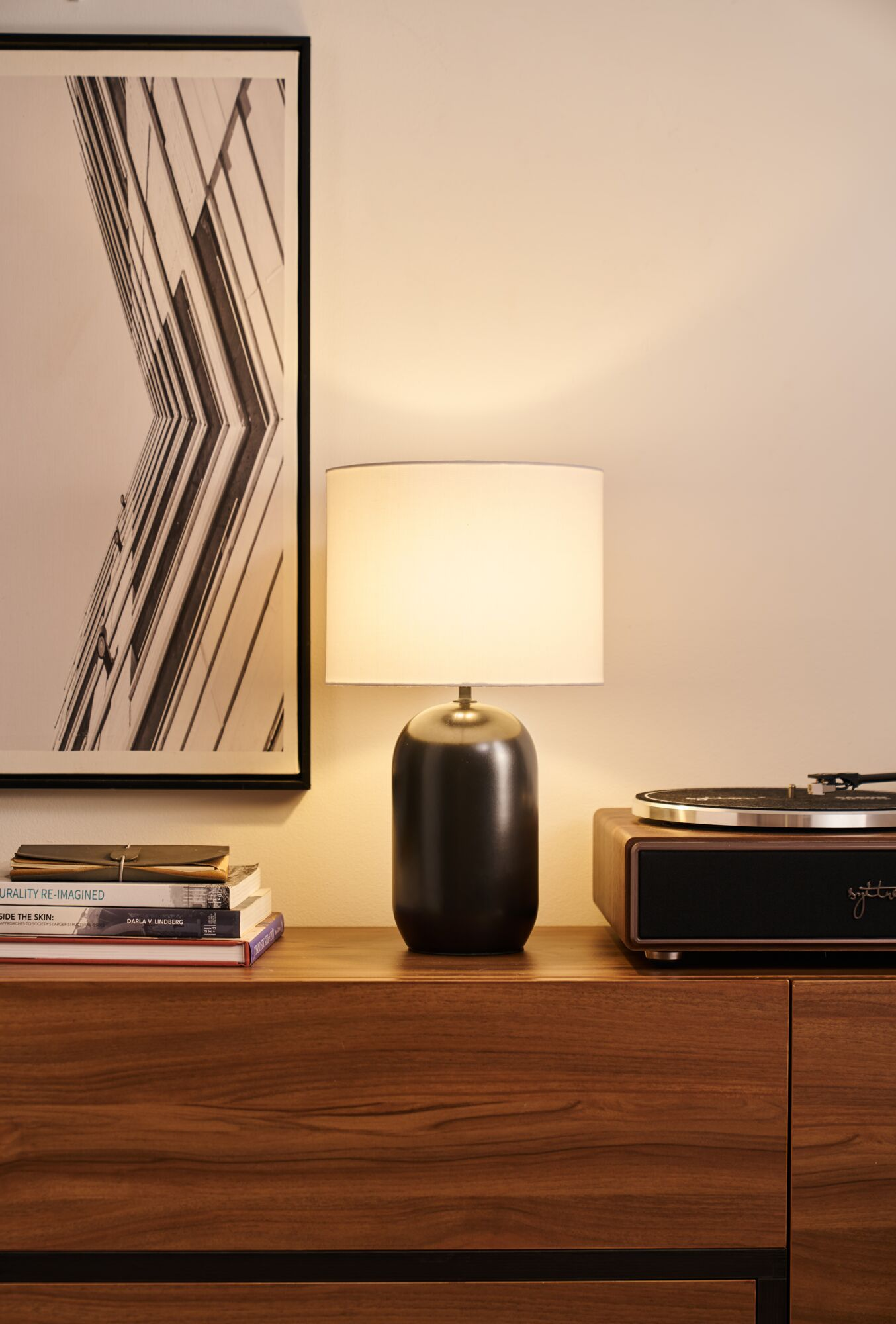 Czarna szafka nocna z lampą, książkami i gramofonem.