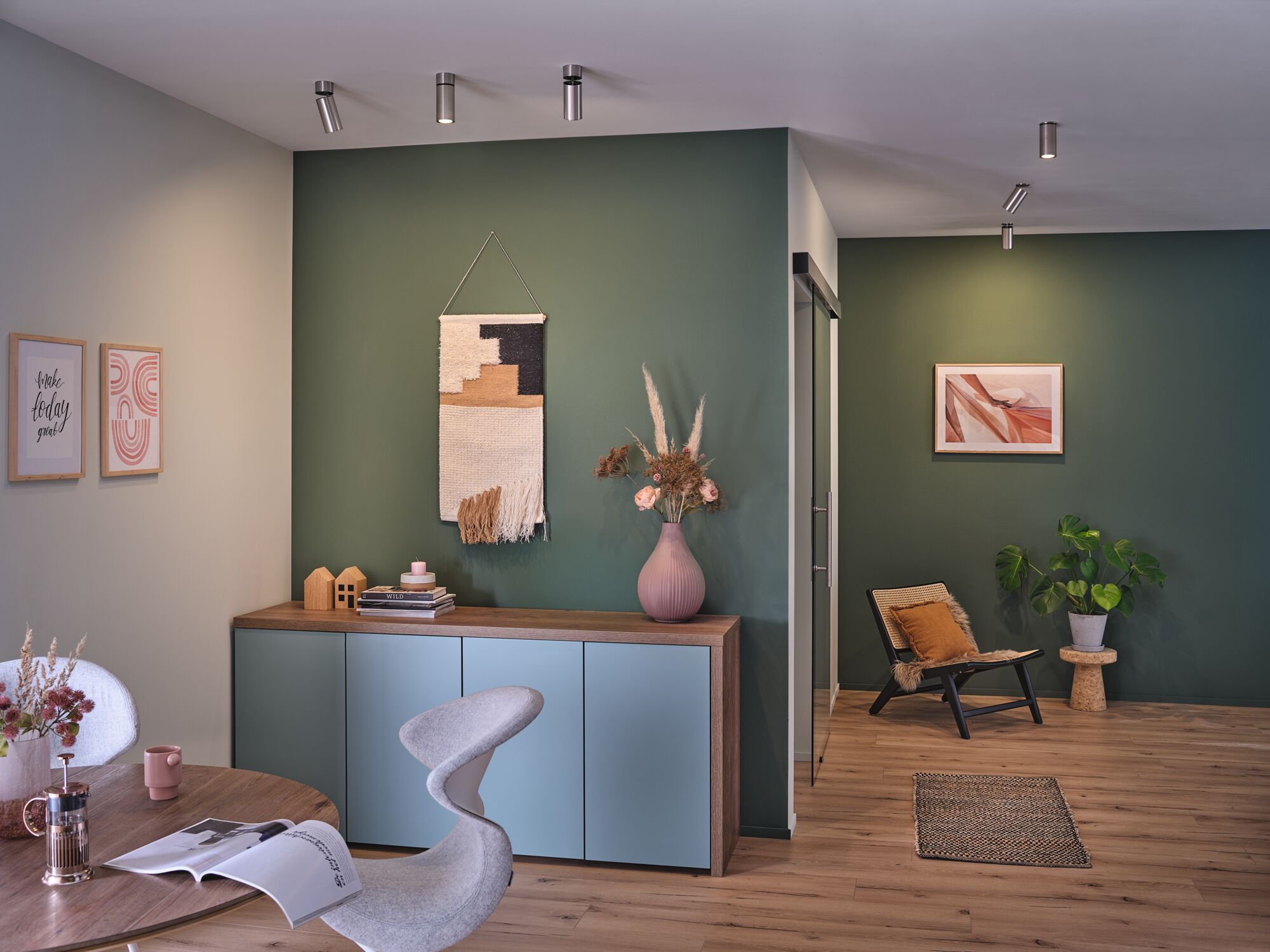 Salon z drewnianą podłogą, zieloną ścianą, szafką, stołem, krzesłem i siedziskiem.