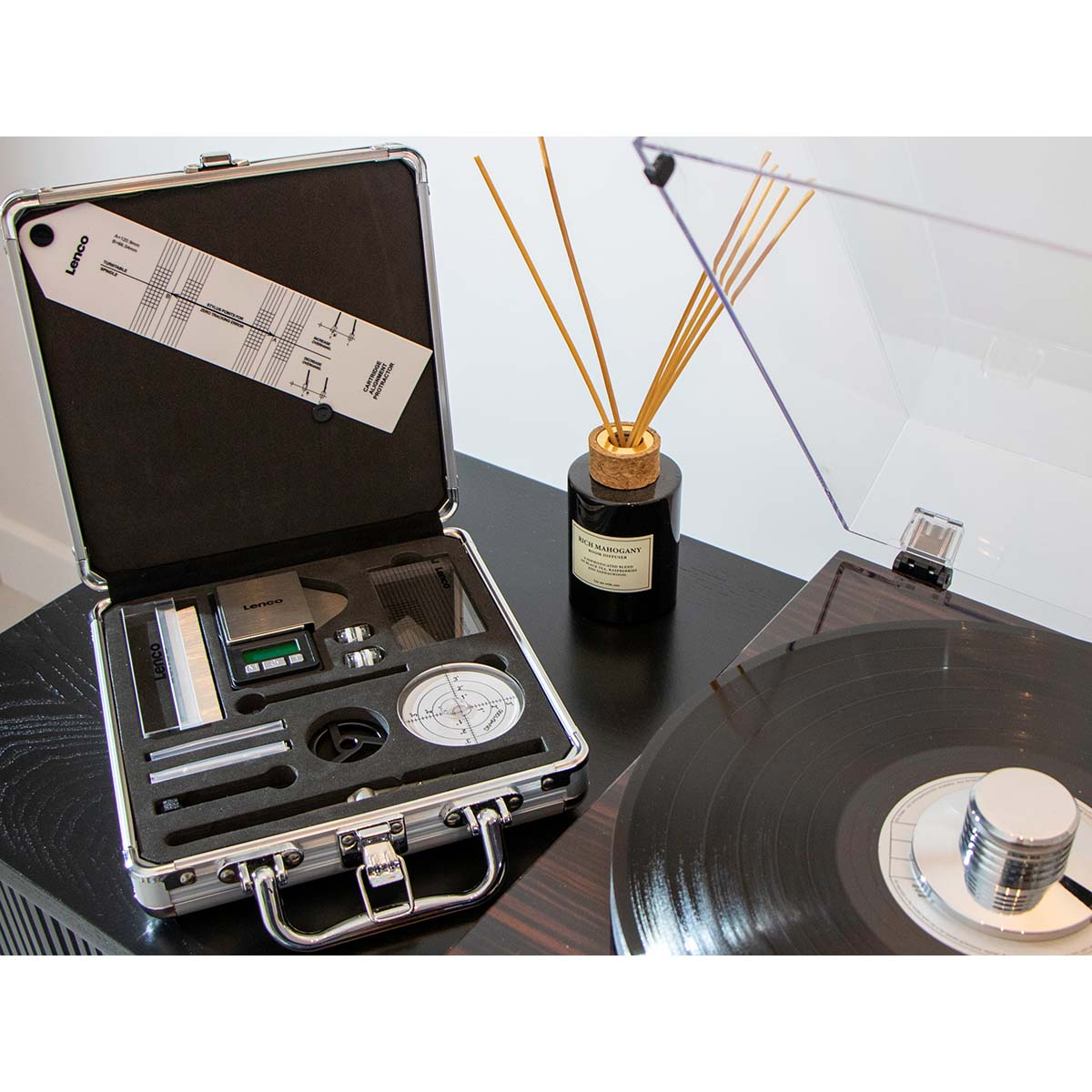 Otwarta walizka z narzędziami, gramofon, dyfuzor na czarnym stole.