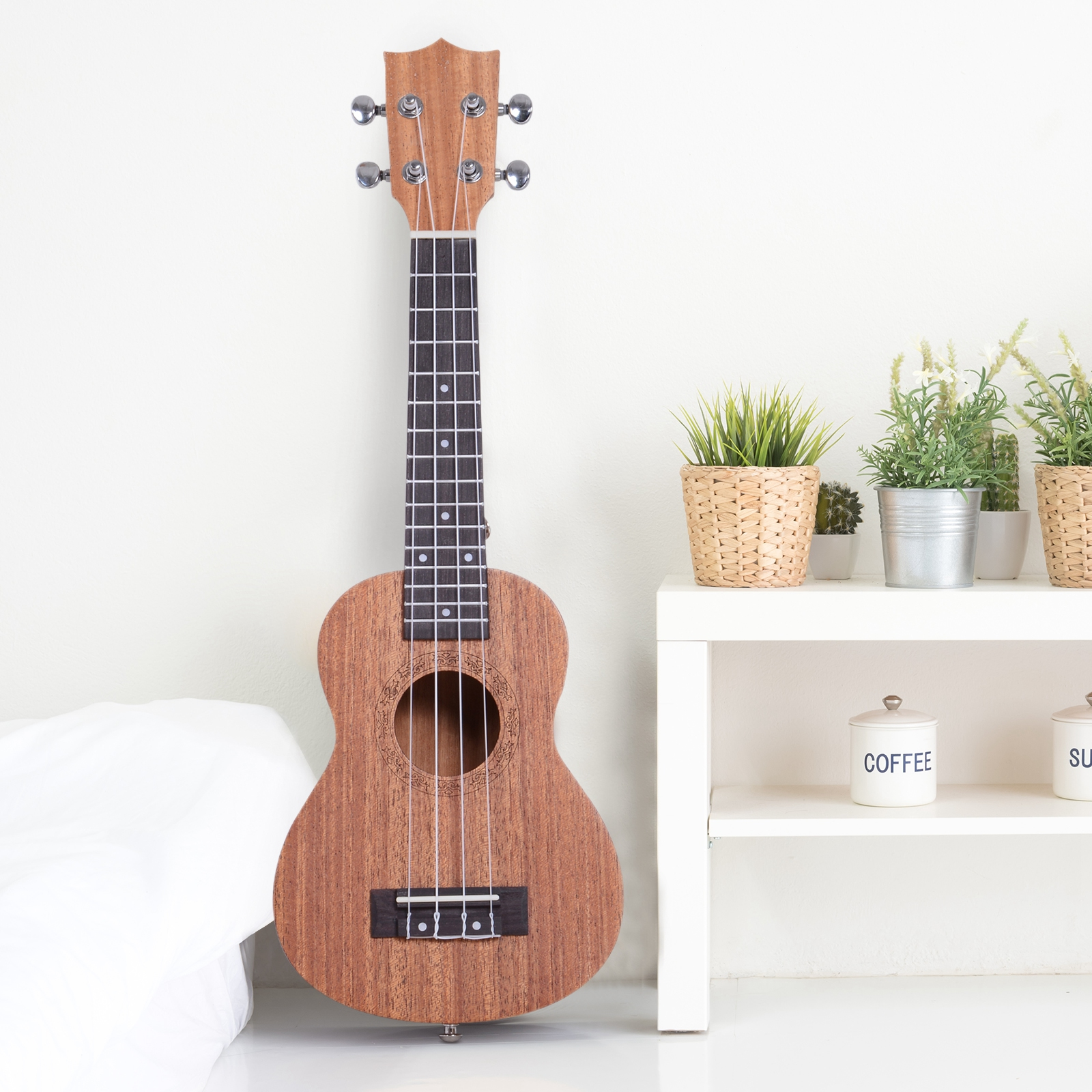 Una ukelele de madera junto a una cama blanca y una estantería con plantas.