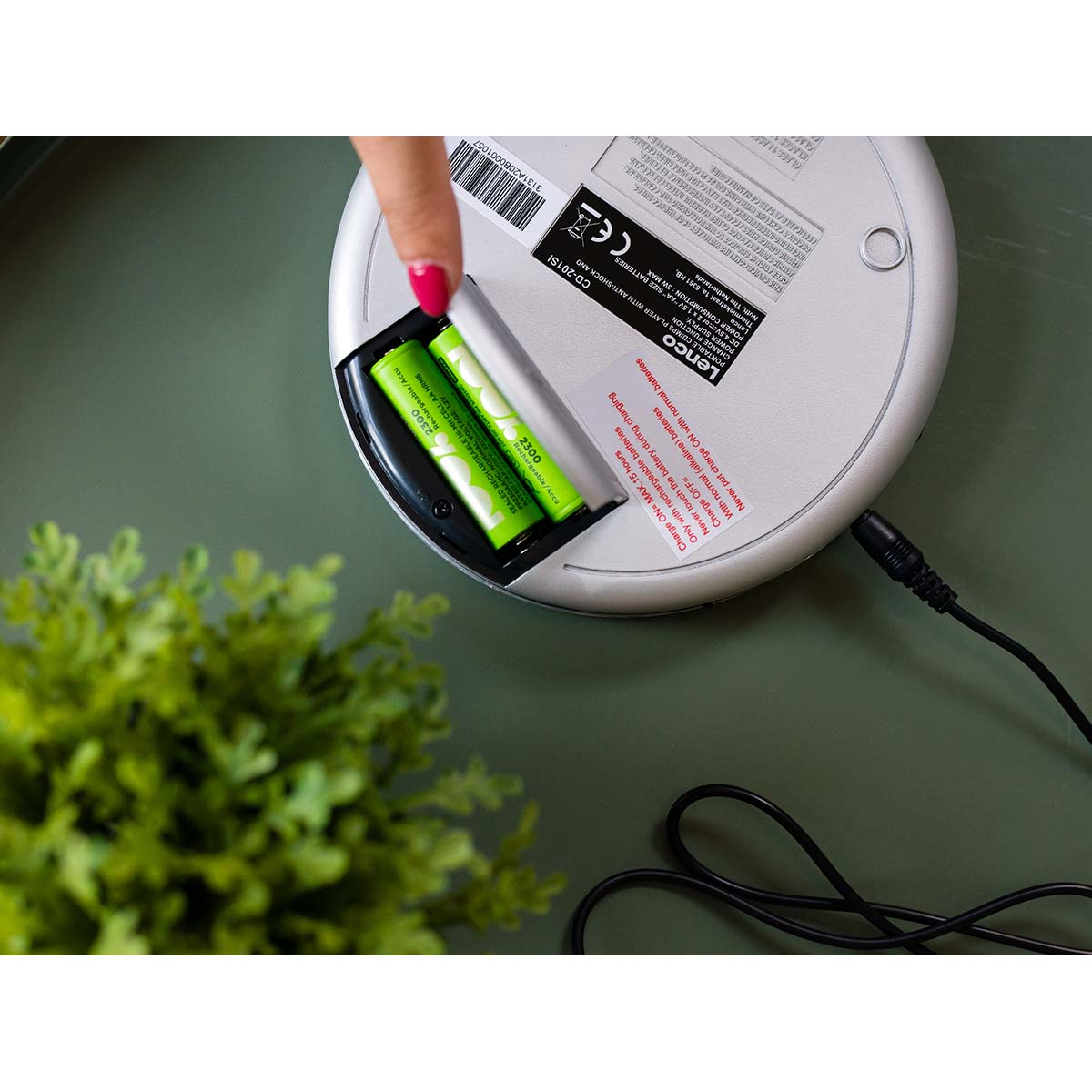 Ręka wkłada dwa zielone akumulatory AA do srebrnego odtwarzacza CD.