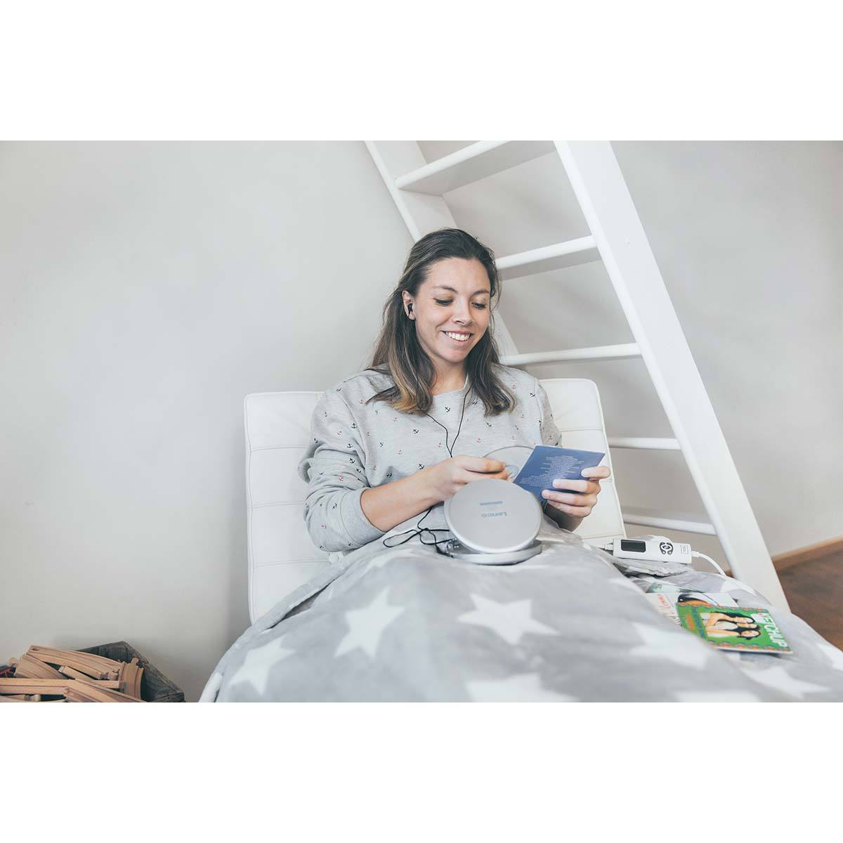 Kobieta siedzi w fotelu, słucha muzyki i czyta książeczkę.