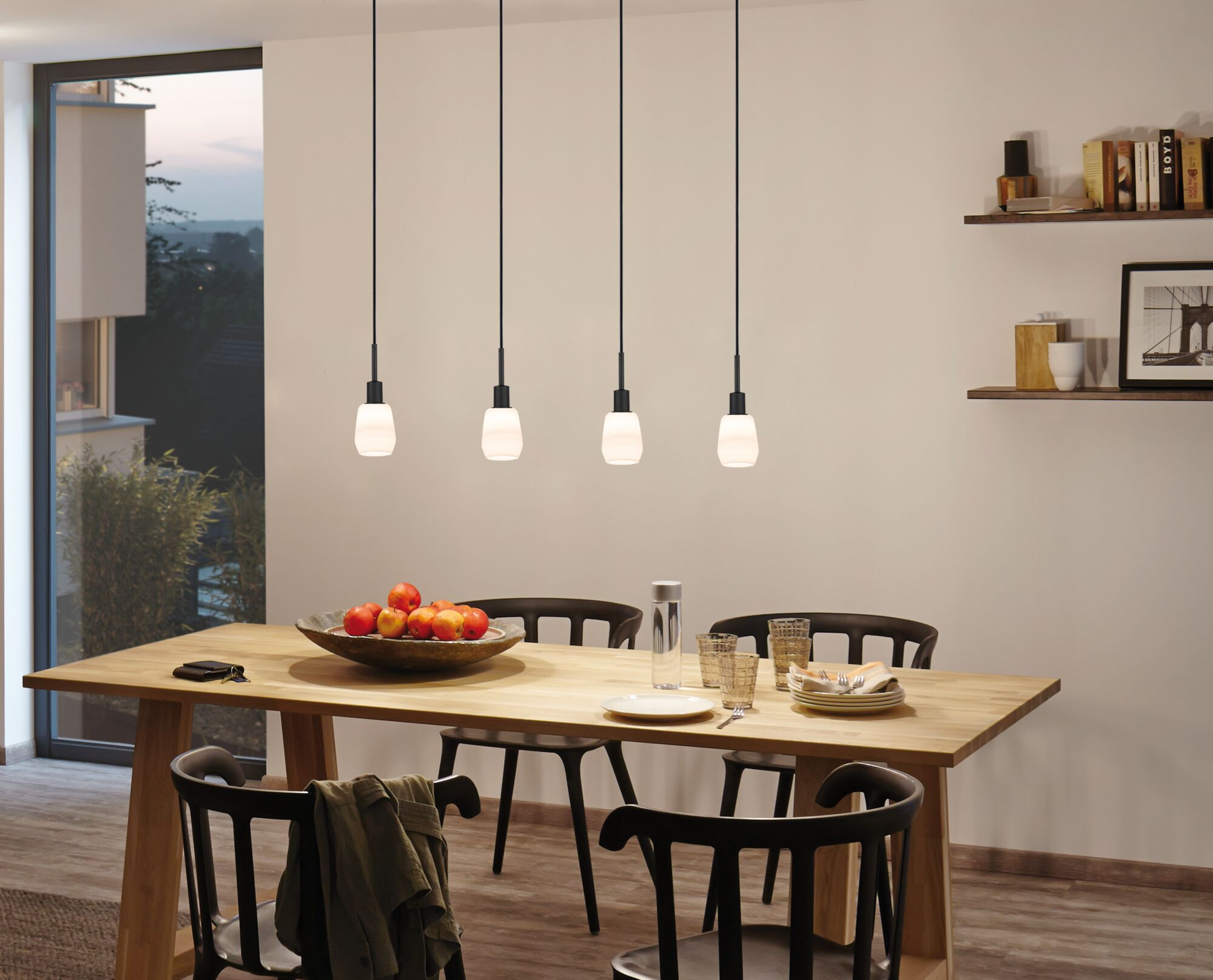Ein Holztisch mit Obstschale, Gläsern und Geschirr, beleuchtet von vier Pendelleuchten.