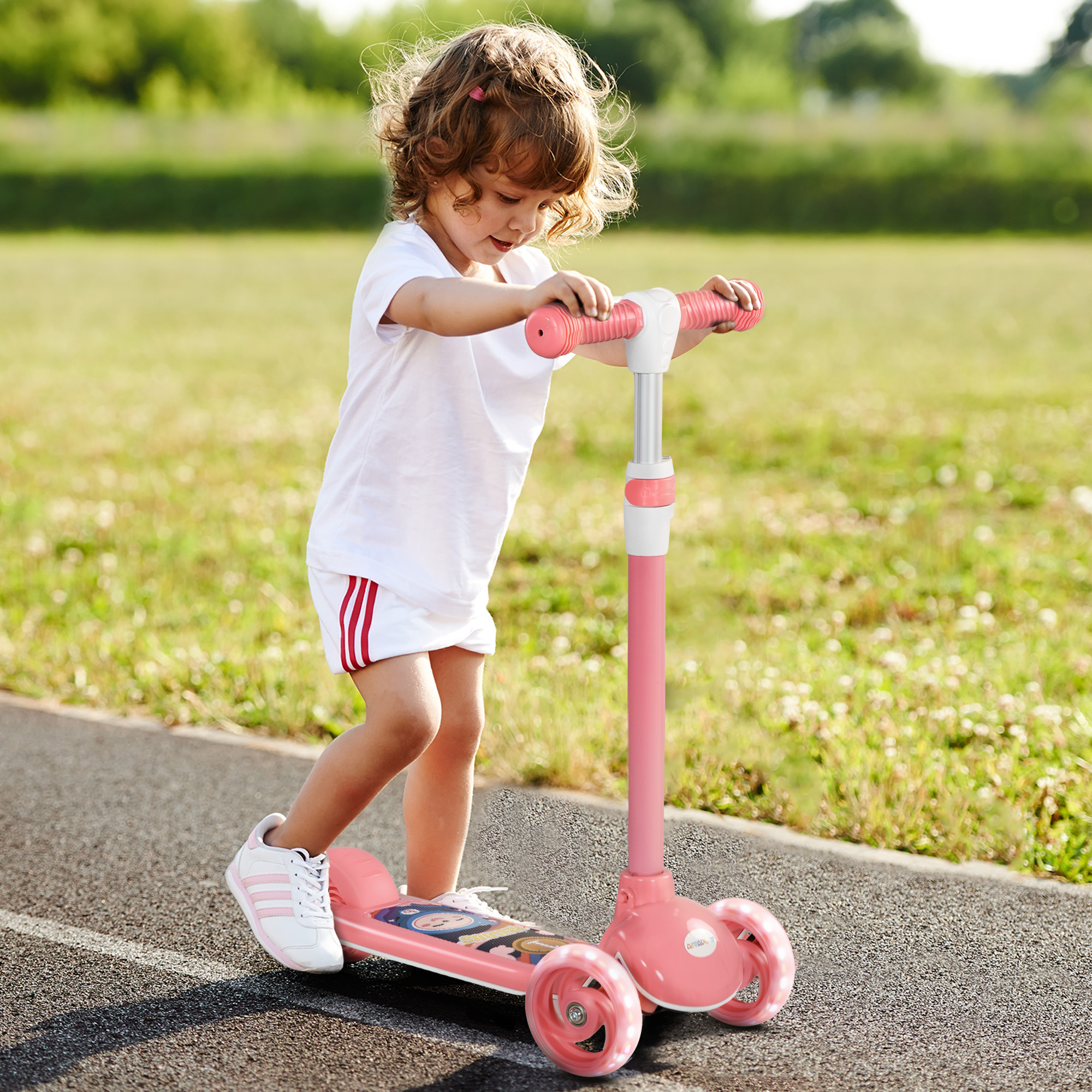 Una niña pequeña con pelo rizado monta un patinete rosa en un camino de asfalto.