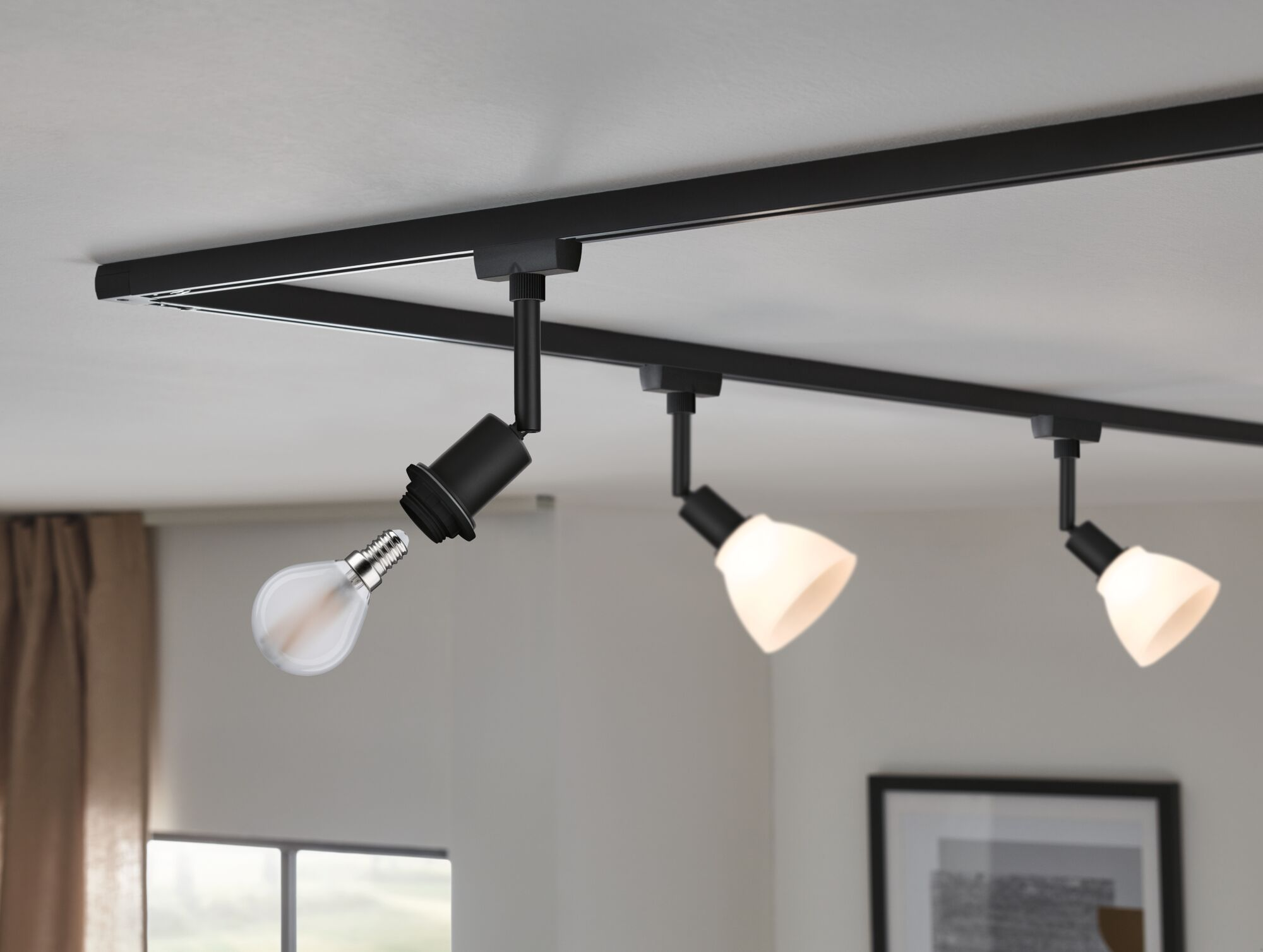 Ein schwarzes Schienensystem an der Decke mit einem leeren Lampenfassung und drei Lampen.