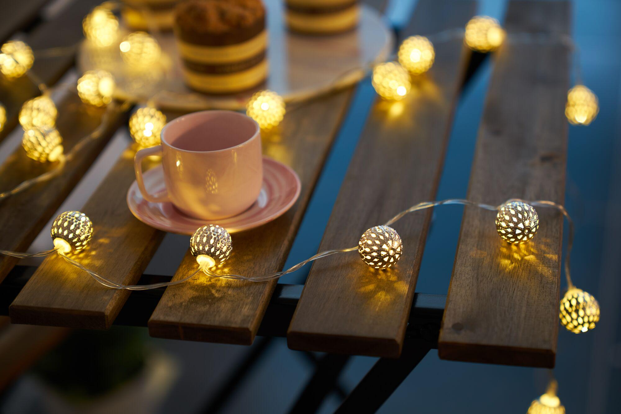 Różowa filiżanka na spodku otoczona lampkami wróżek na drewnianym stole.