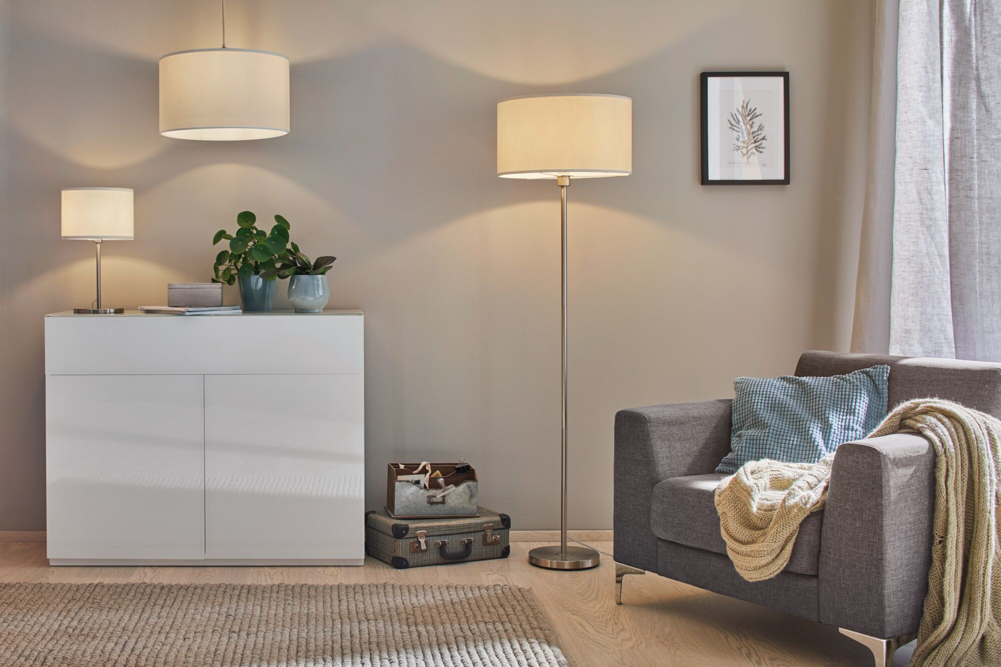 Ein Sessel mit Kissen und Decke neben Stehlampe und Kommode.