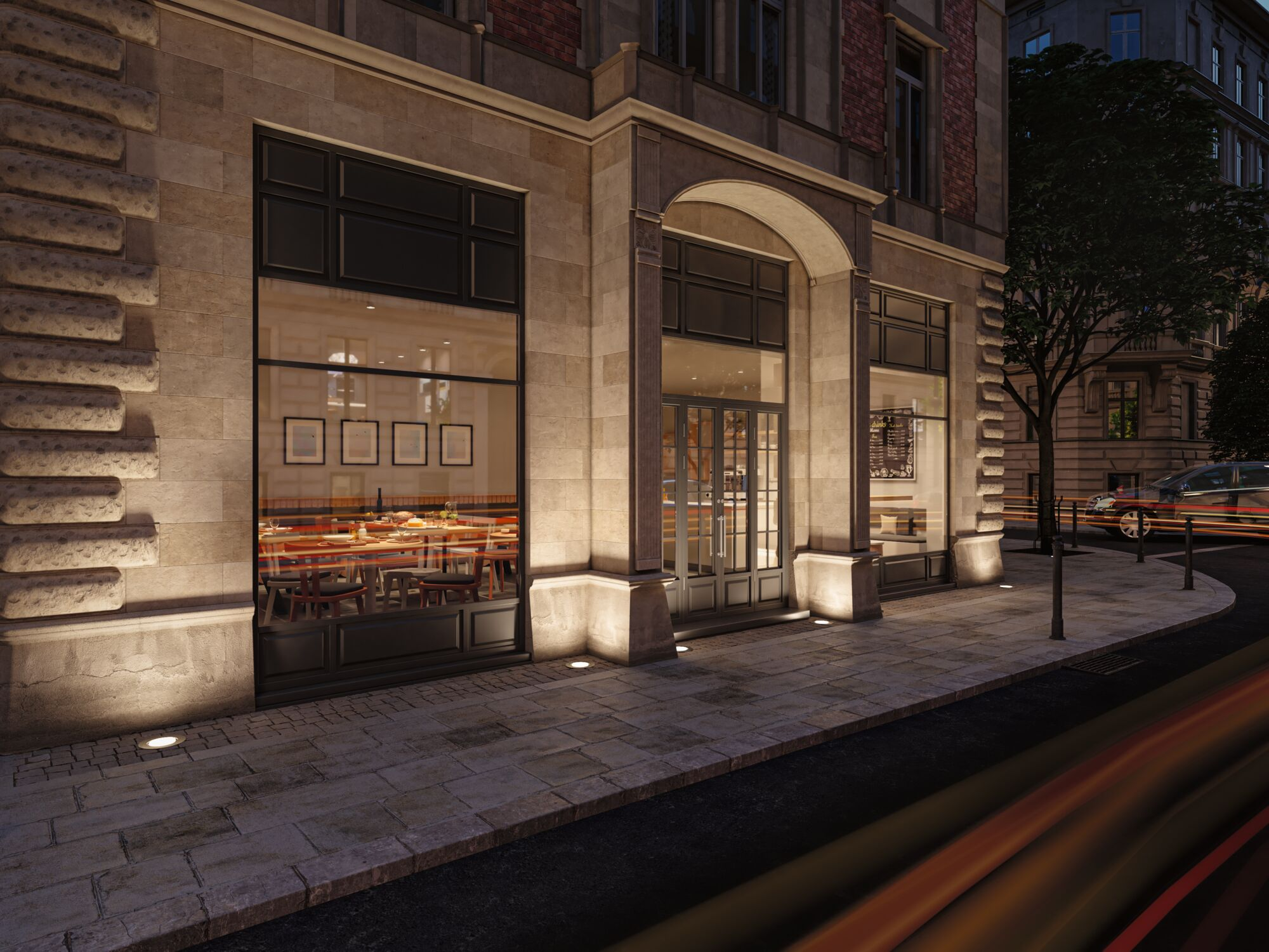 Fasada restauracji nocą z oświetlonym chodnikiem i przejeżdżającym samochodem.