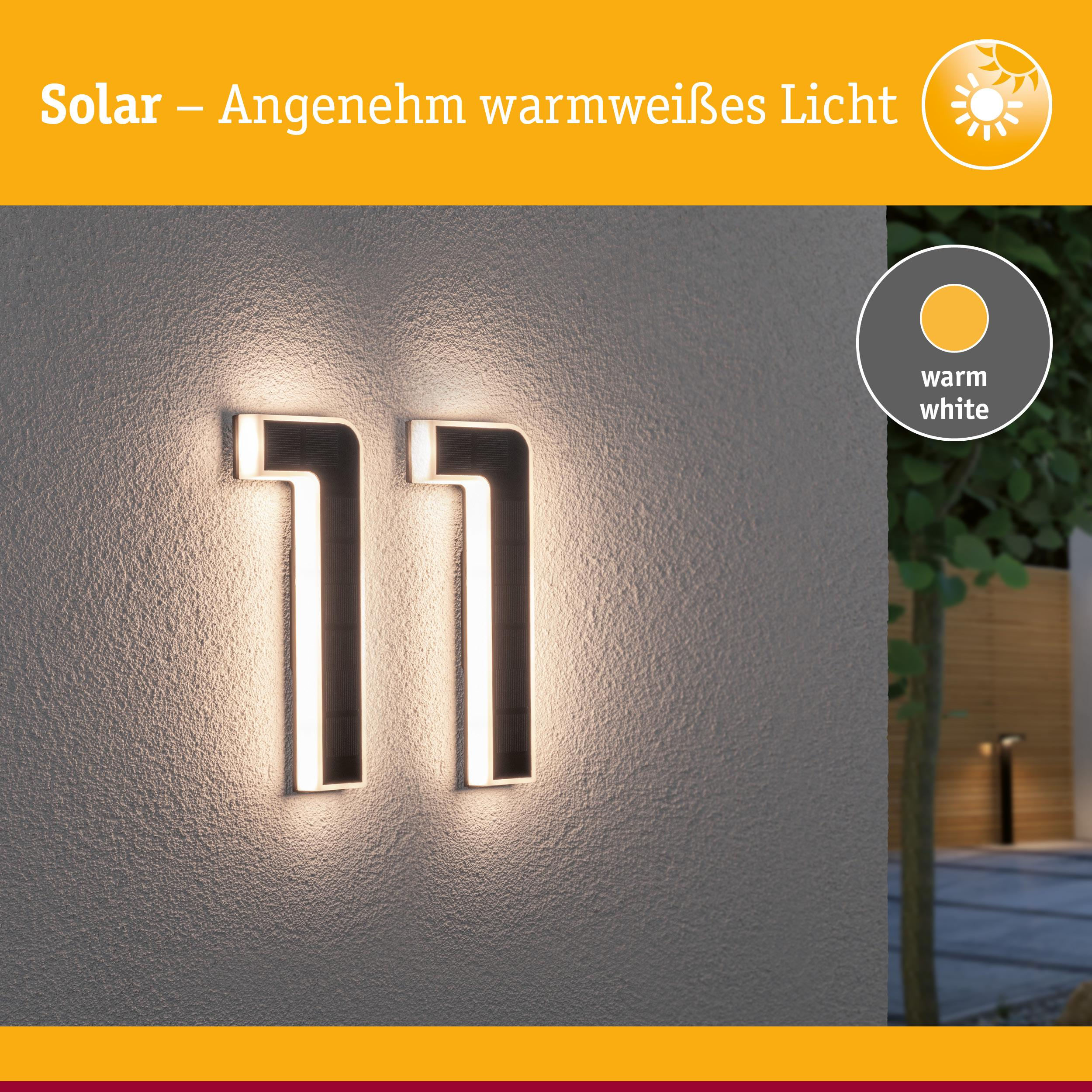 Zewnętrzna lampa solarna nr 11 świeci ciepłą bielą na szarej ścianie.