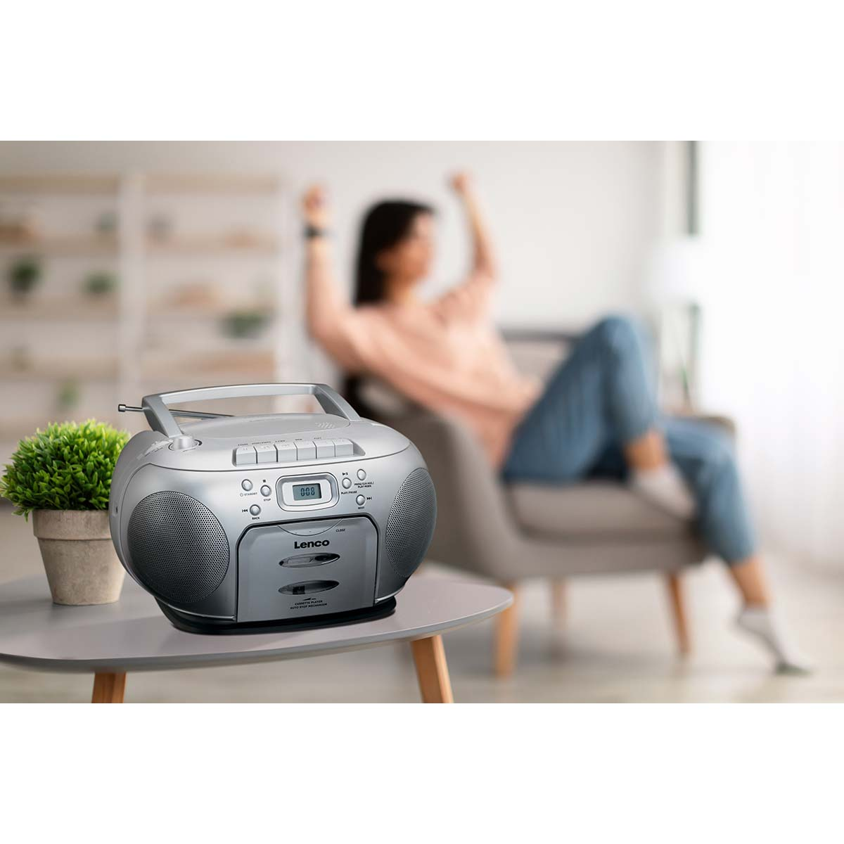 Une boombox argentée sur une table, une femme danse en arrière-plan.