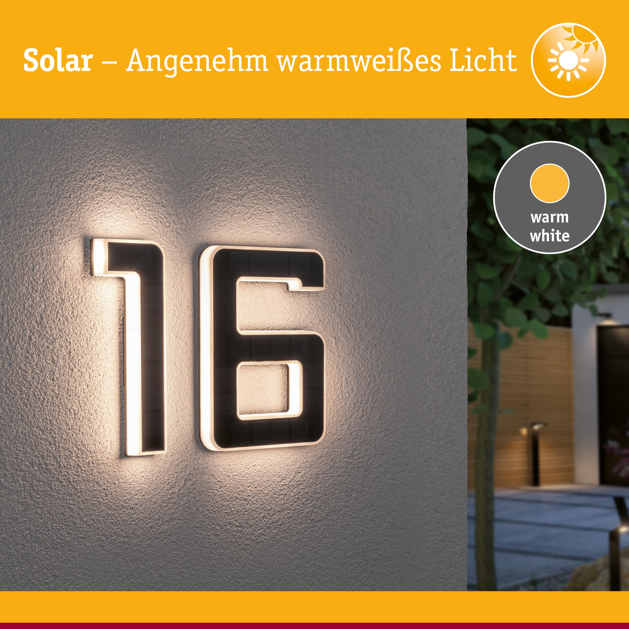 Numer domu solarny 16 świeci na biało-ciepło na ścianie, z ogrodem w tle.