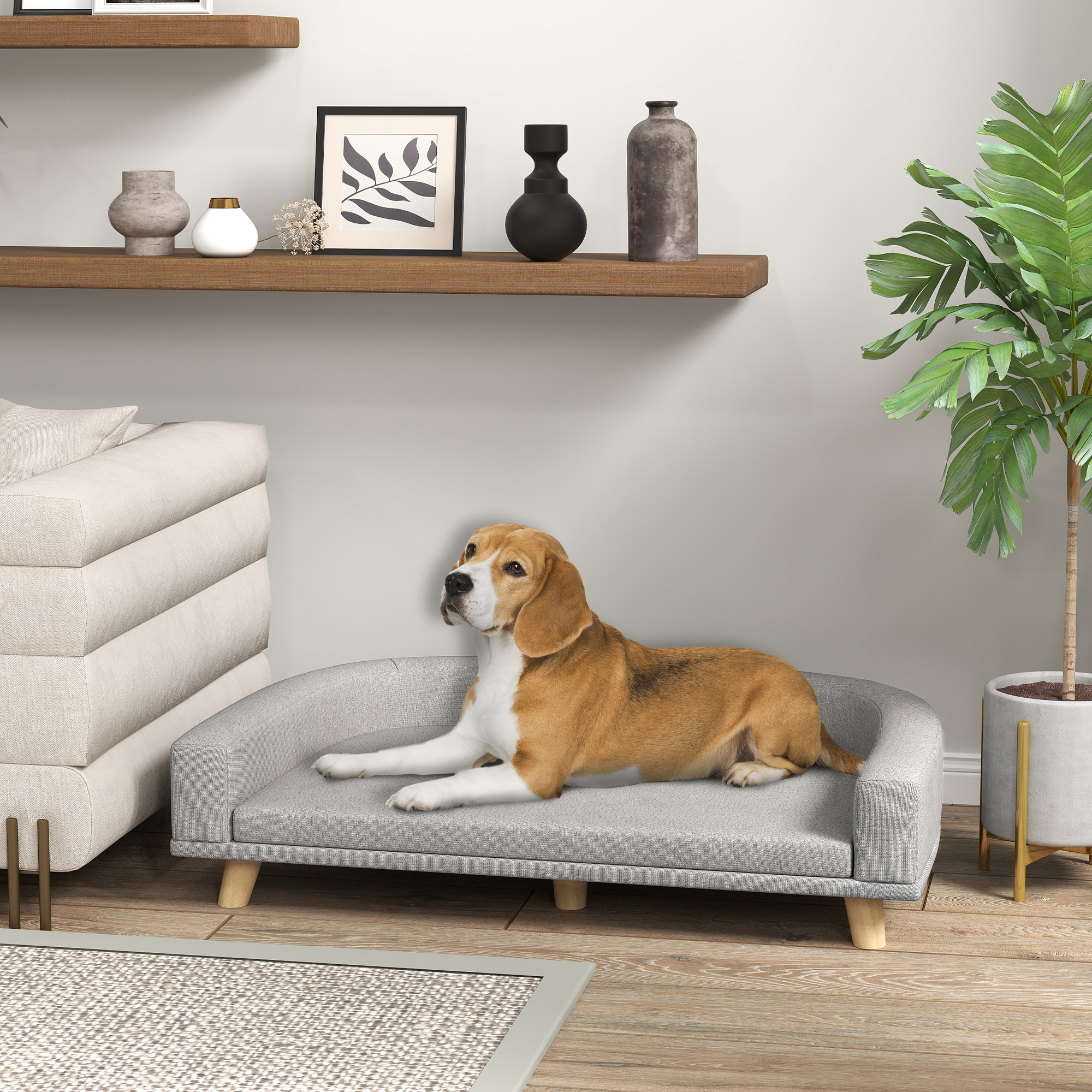 Un beagle descansa en una cama para perros gris, cerca de un sofá y una planta.