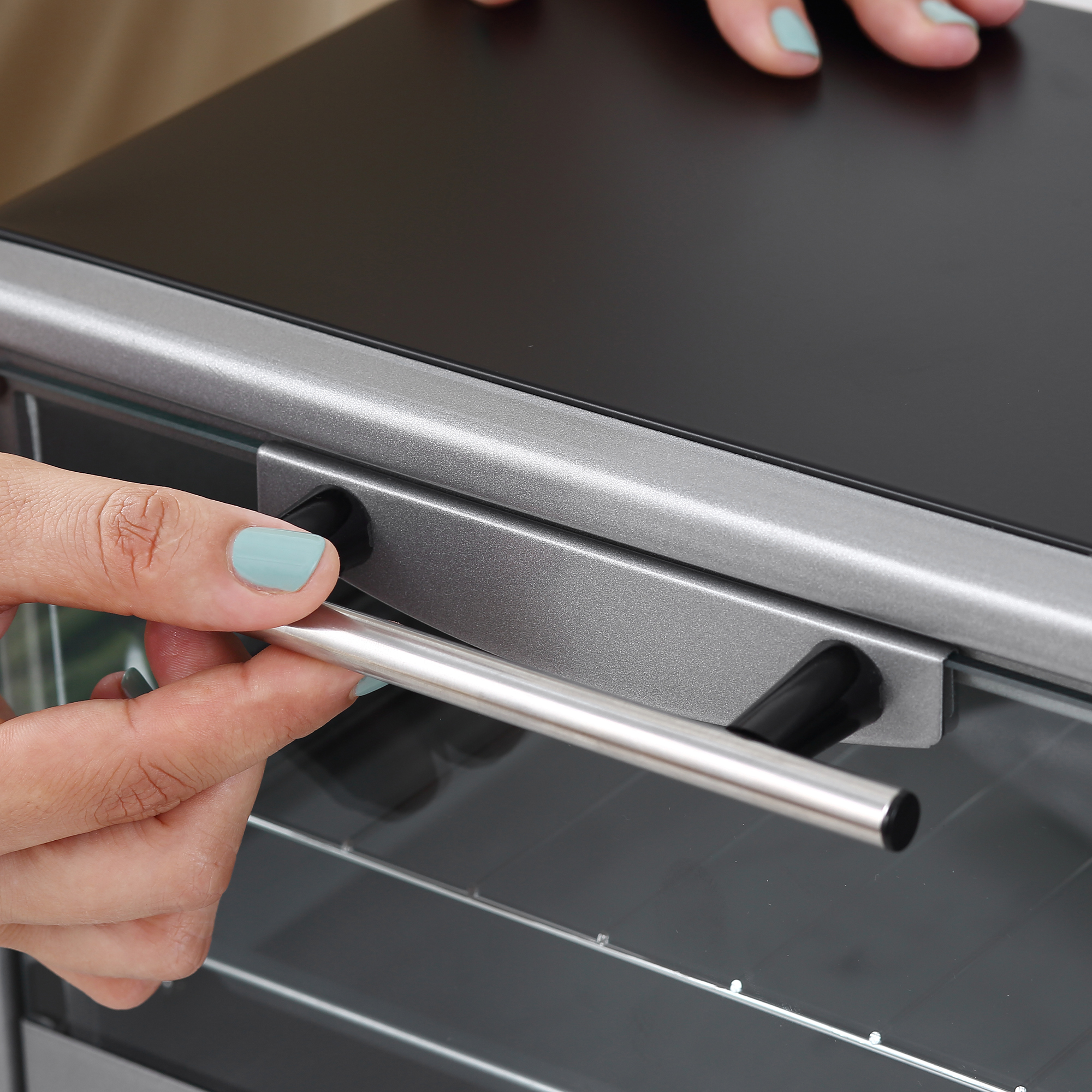 Una mano con uñas azul claro abre el tirador plateado de un horno negro.