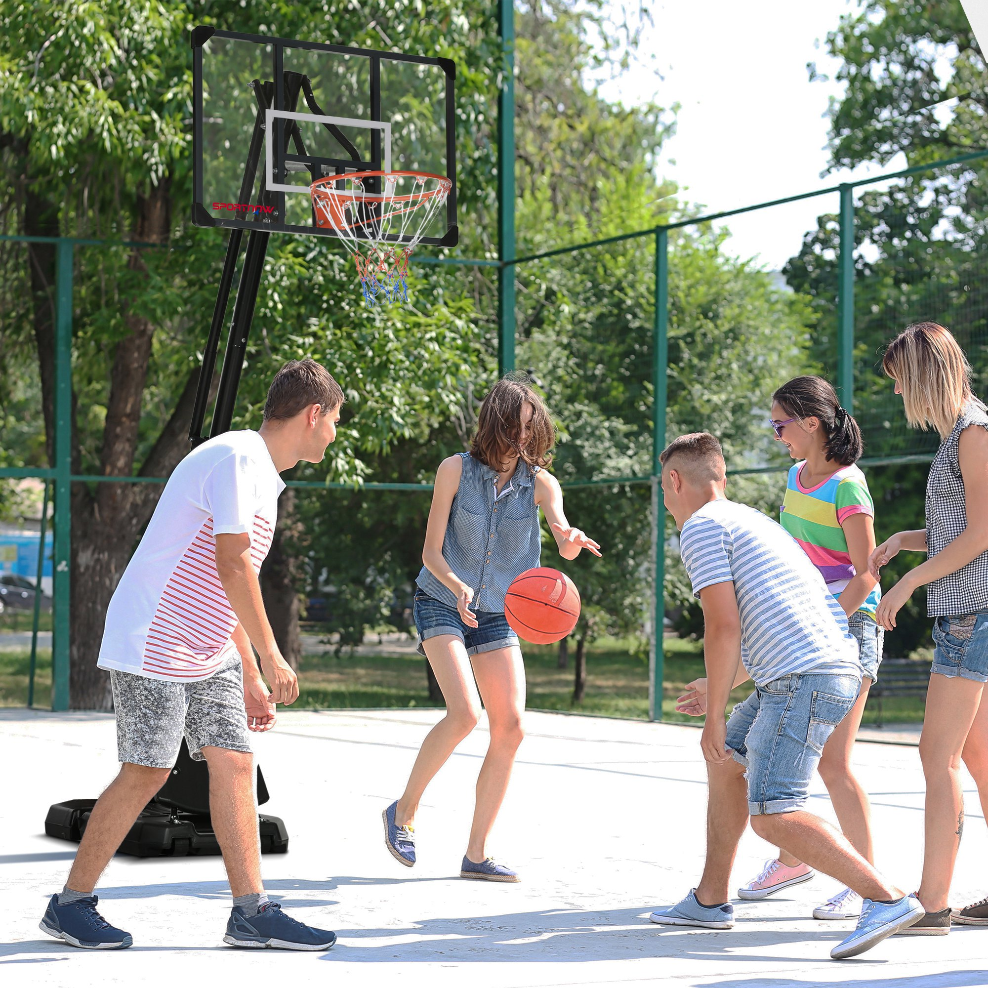 Cinco jóvenes juegan al baloncesto en una cancha al aire libre con árboles de fondo.
