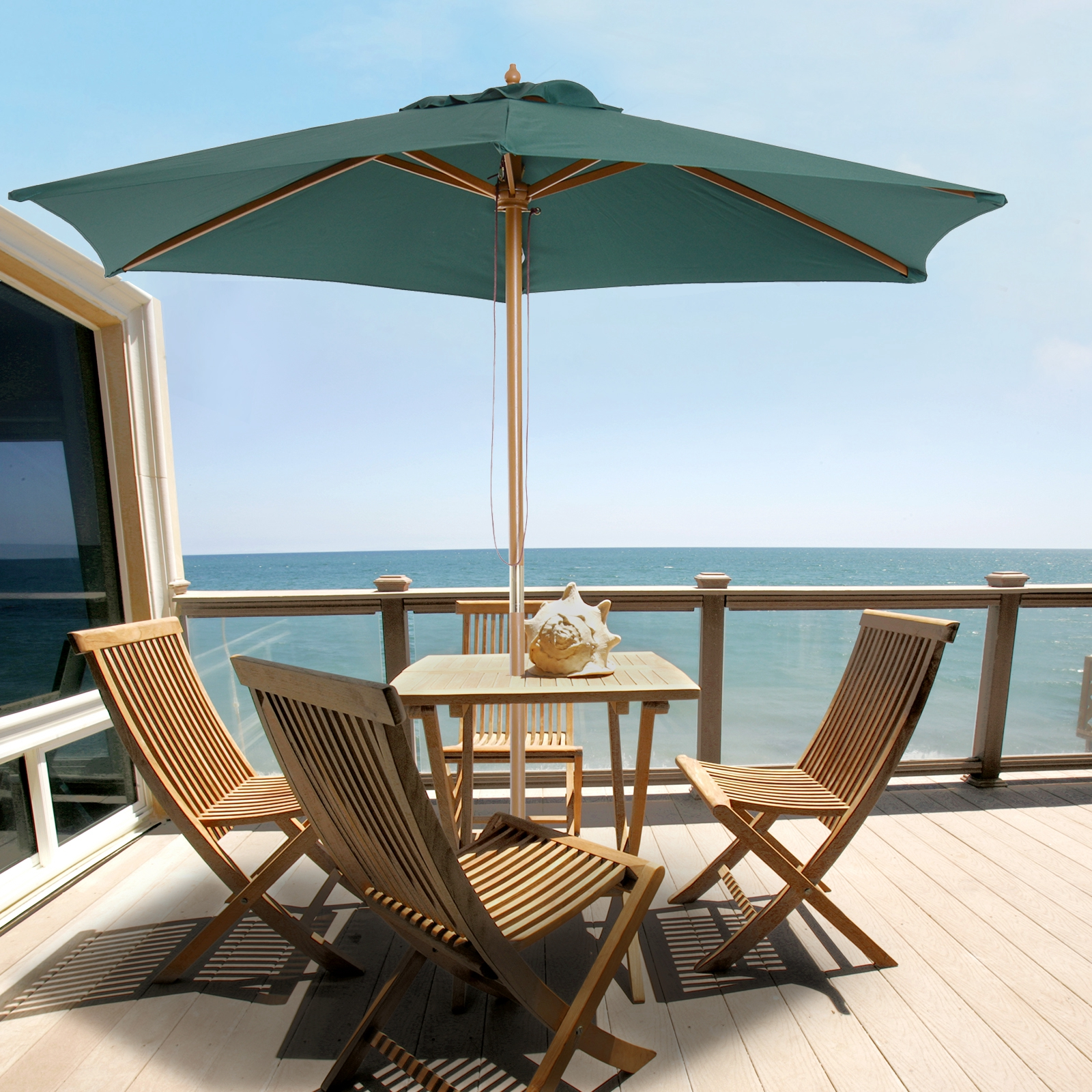 Muebles de madera en una terraza con vistas al mar bajo una sombrilla.