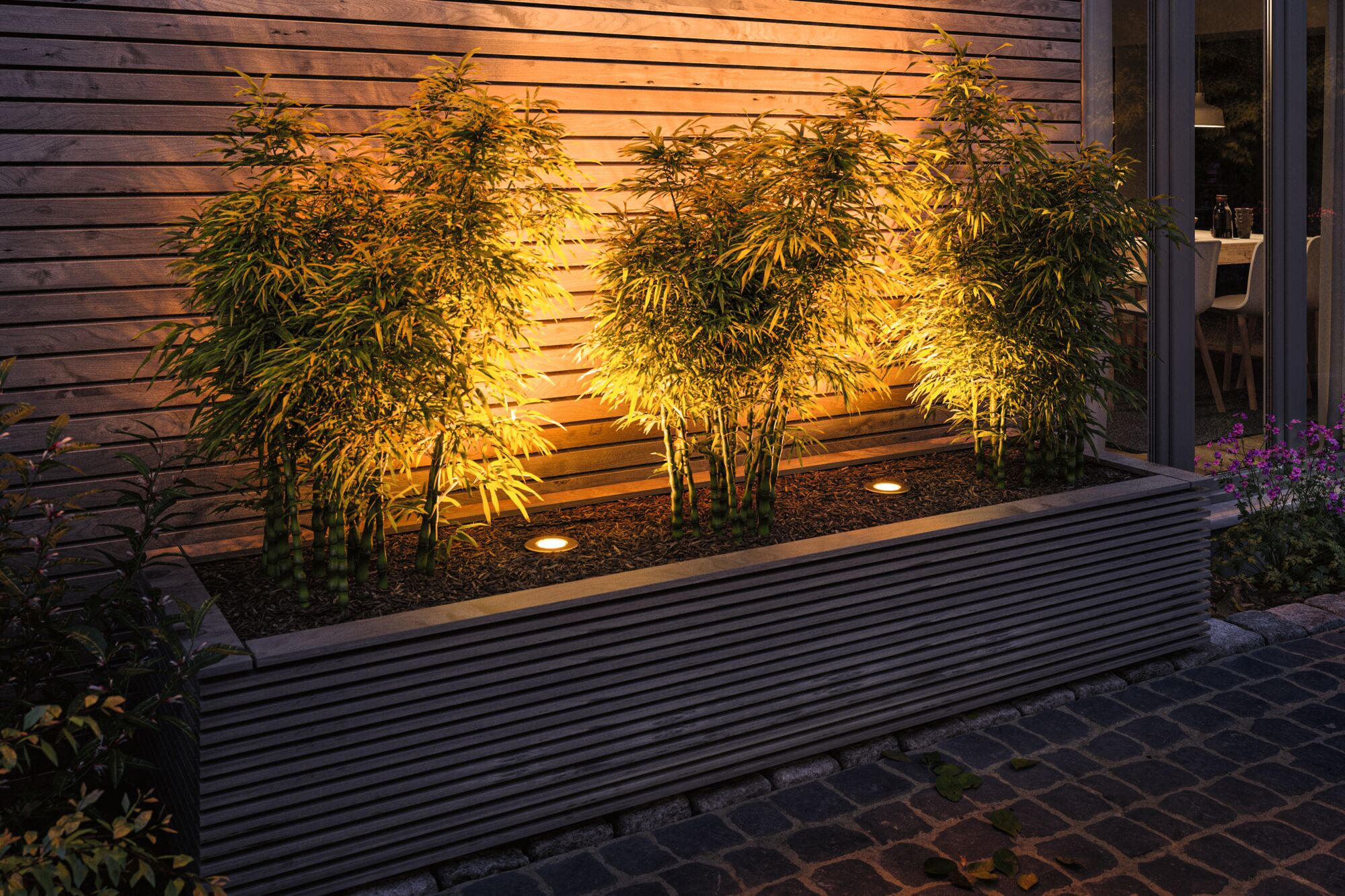 Bambou éclairé dans une jardinière en bois devant un mur en bois la nuit.
