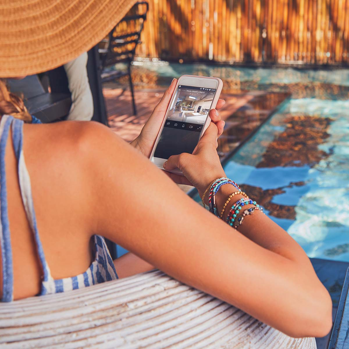 Eine Frau mit Hut schaut auf ihr Handy, das eine Überwachungskamera anzeigt.
