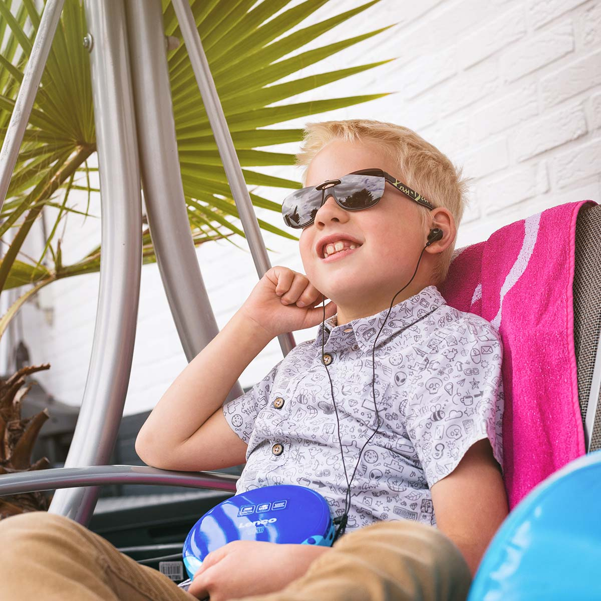 Chłopiec w okularach przeciwsłonecznych i słuchawkach siedzi na huśtawce, słuchając muzyki.