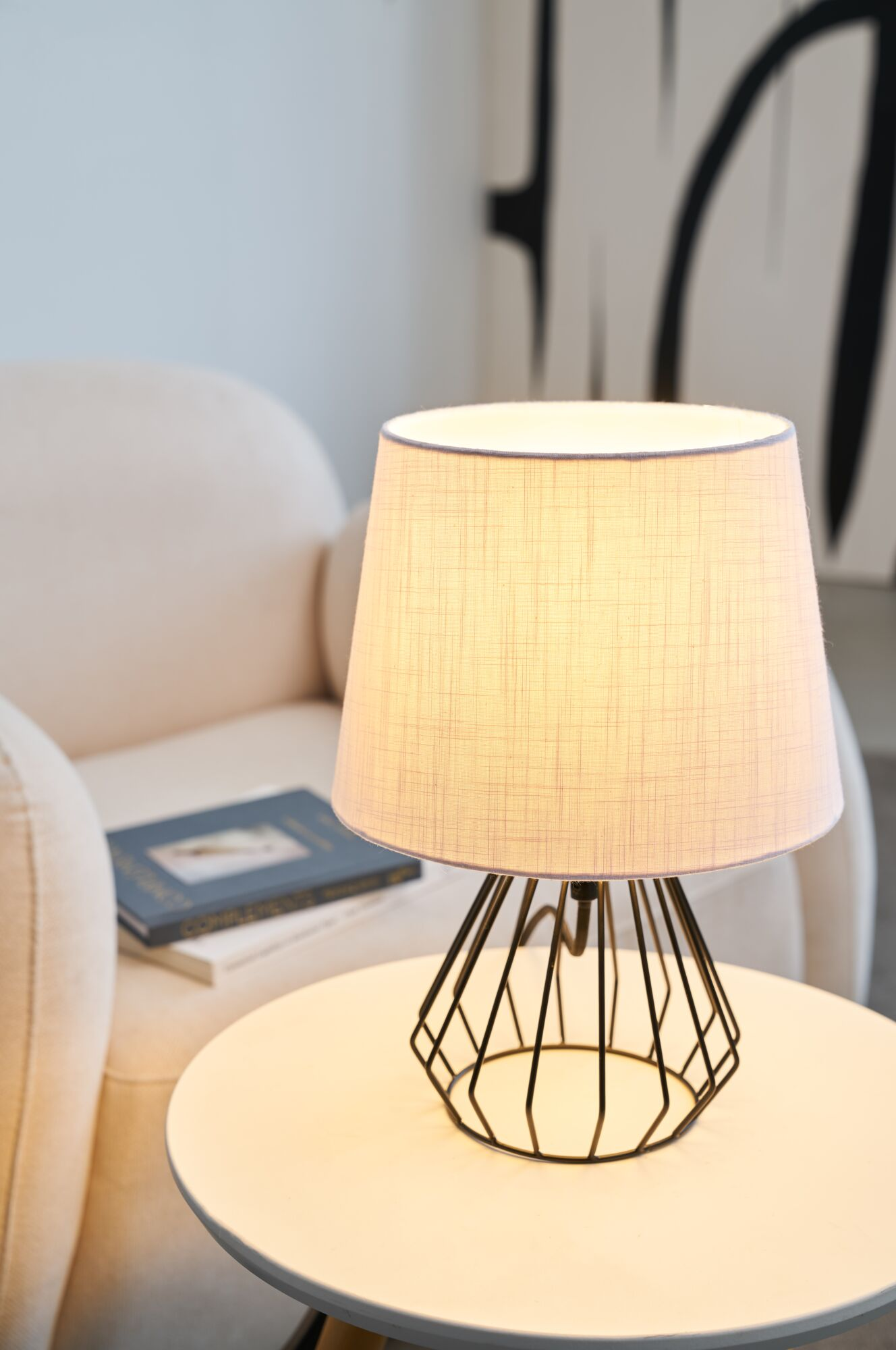 Lampa z drucianym stelażem stoi na stole obok fotela.