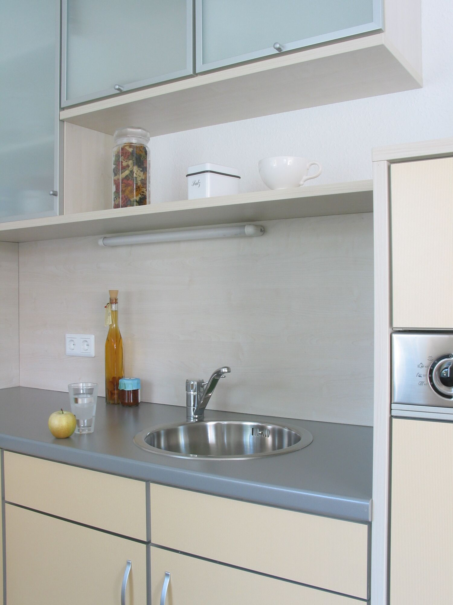 Eine Küche mit Spüle, Wasserhahn, Glas, Apfel, Flasche und Schrank.