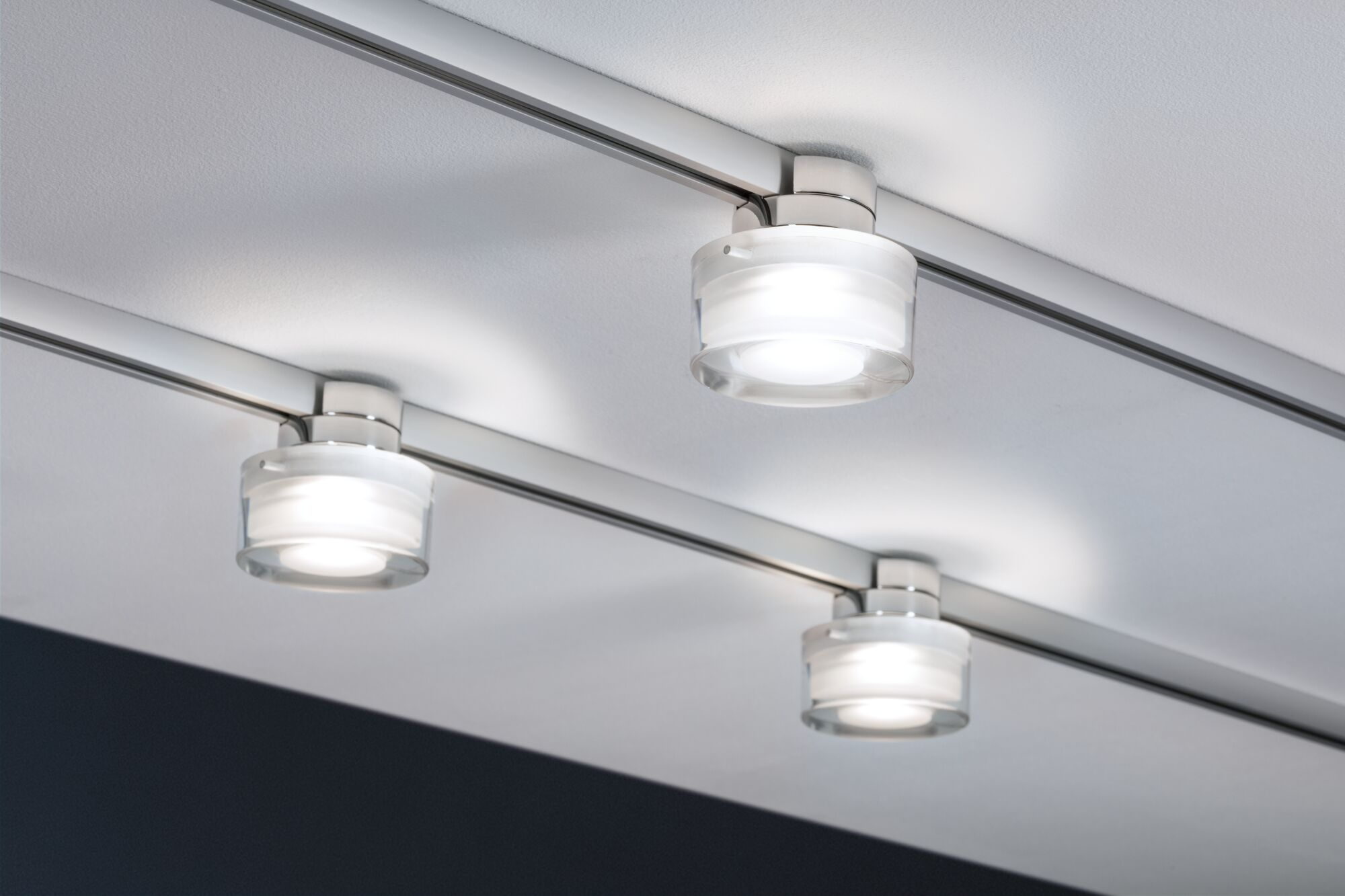 Drei moderne Deckenleuchten mit Glasdiffusoren auf einer Metallschiene.