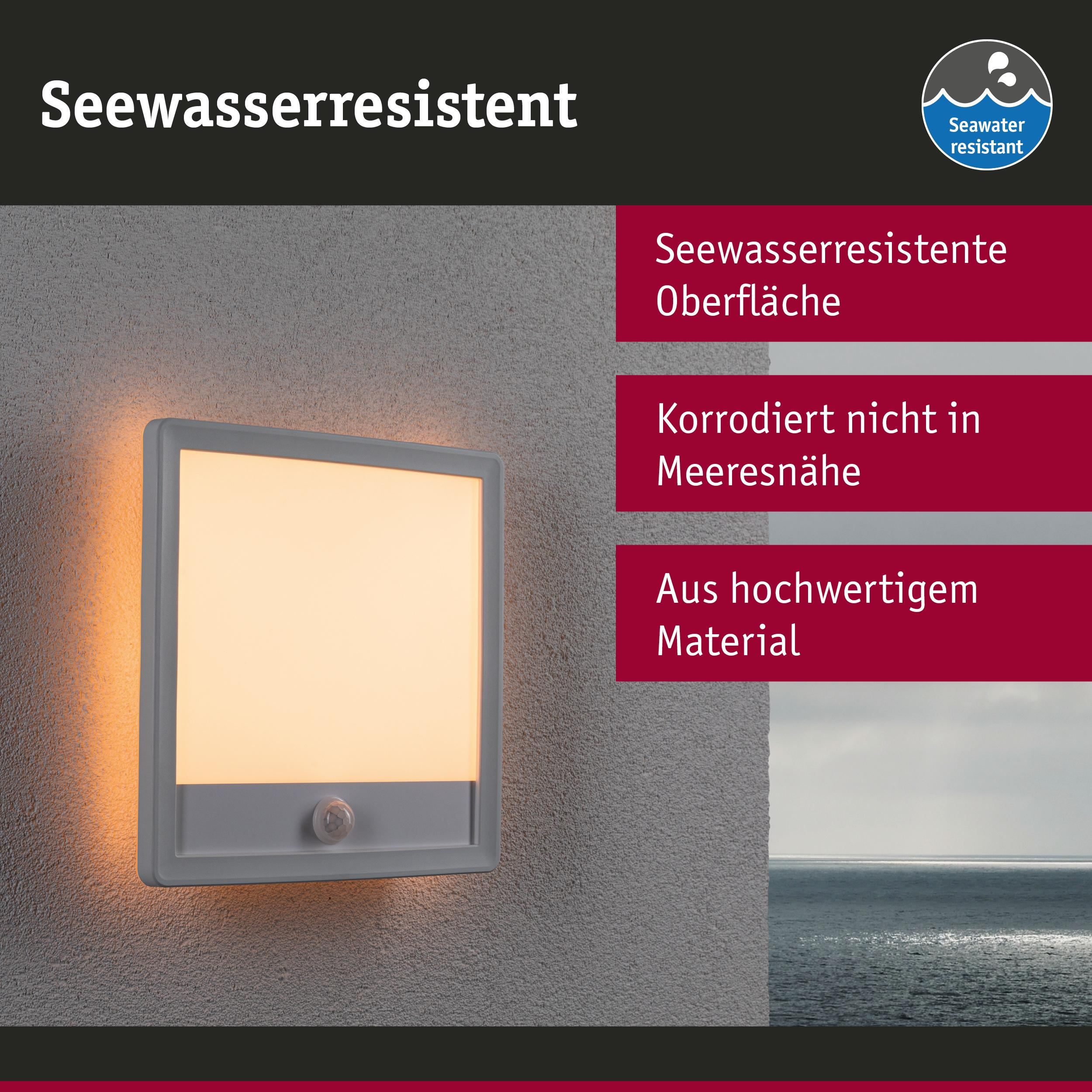 Graue Wandlampe mit Bewegungsmelder leuchtet warmweiß, Meer im Hintergrund.