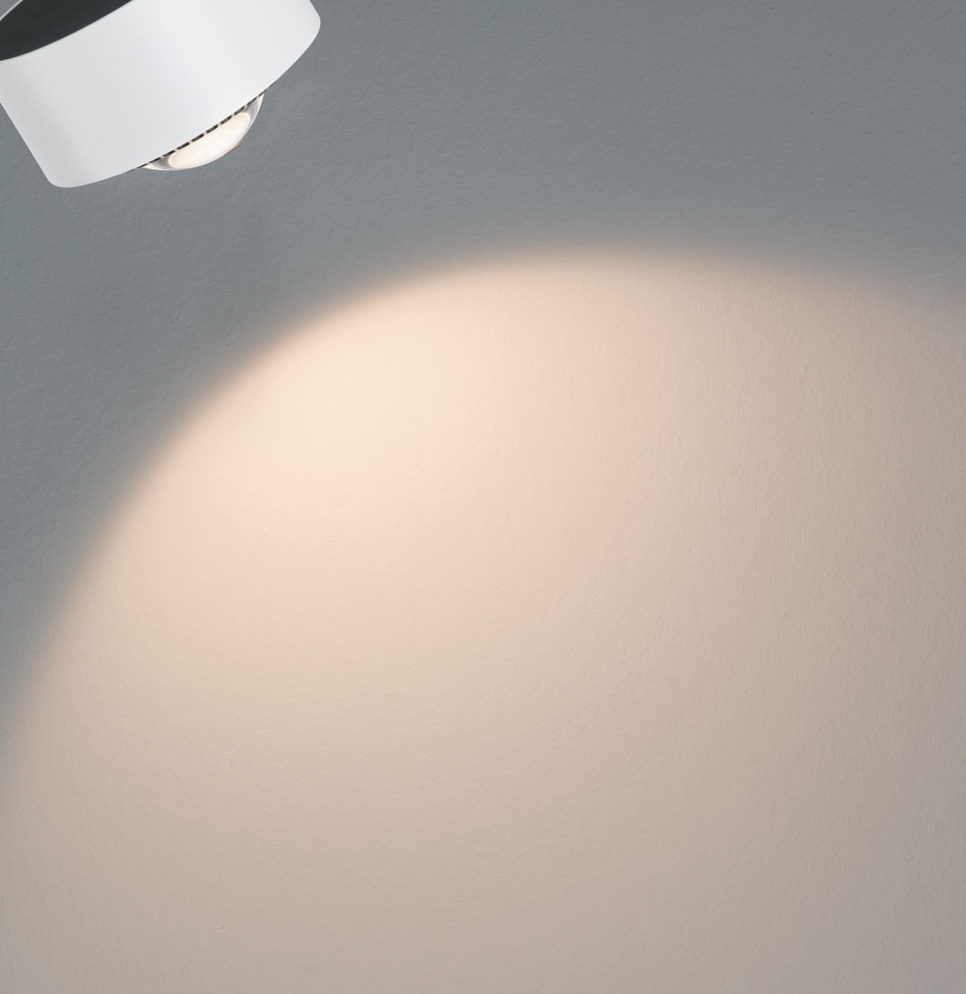 Ein weißer Strahler beleuchtet eine Wand mit einem warmen Lichtkreis.
