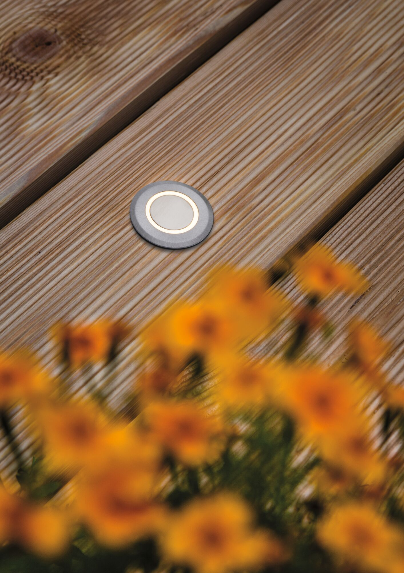 Ein eingelassener Leuchter auf Holzplanken mit unscharfen gelben Blumen im Vordergrund.
