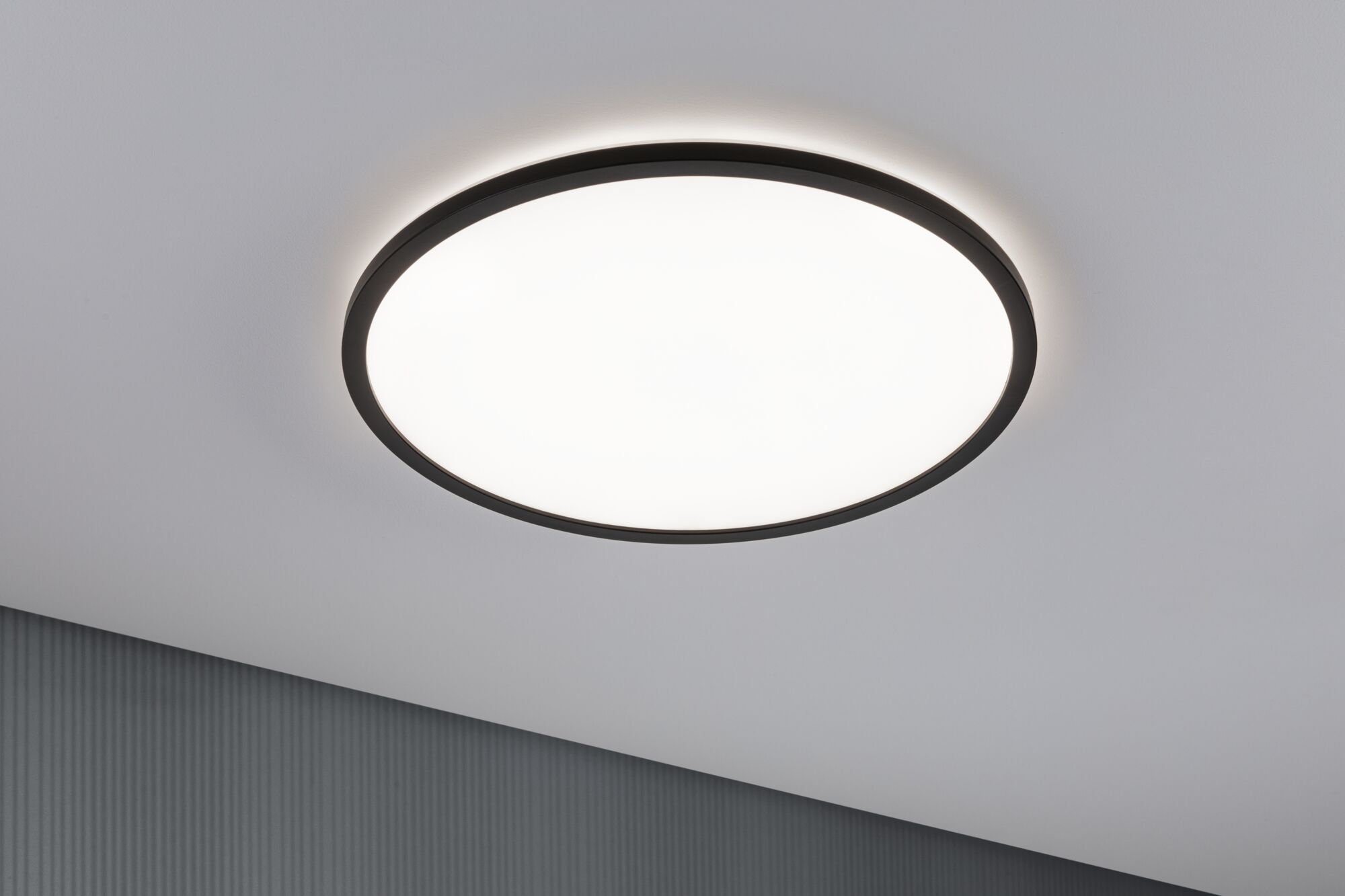 Una plafoniera rotonda con cornice nera illumina il soffitto bianco.