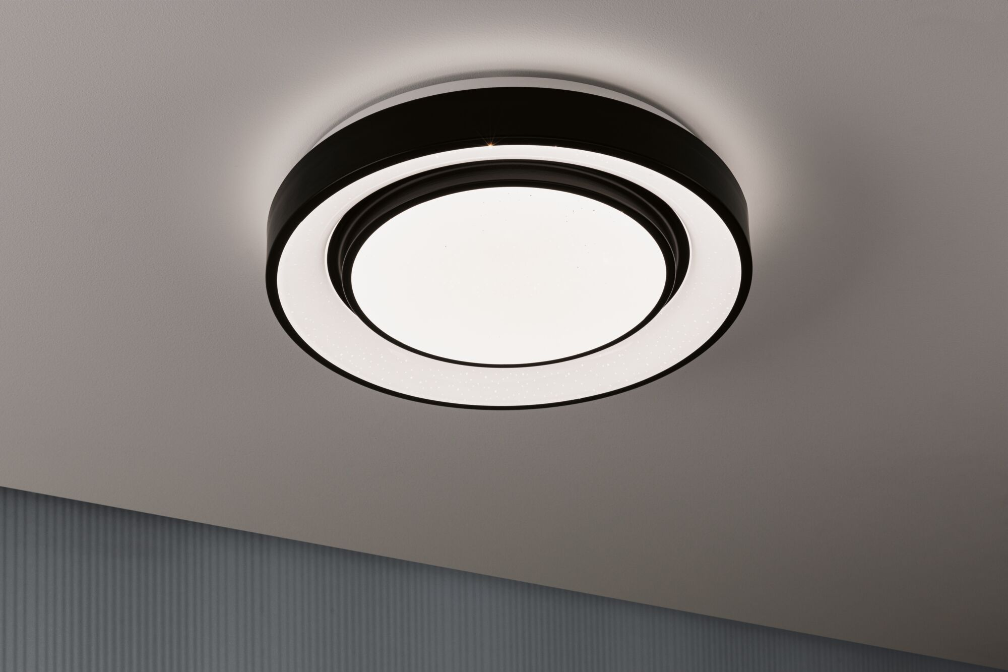 Un plafonnier moderne avec deux anneaux noirs et un cercle intérieur éclairé.