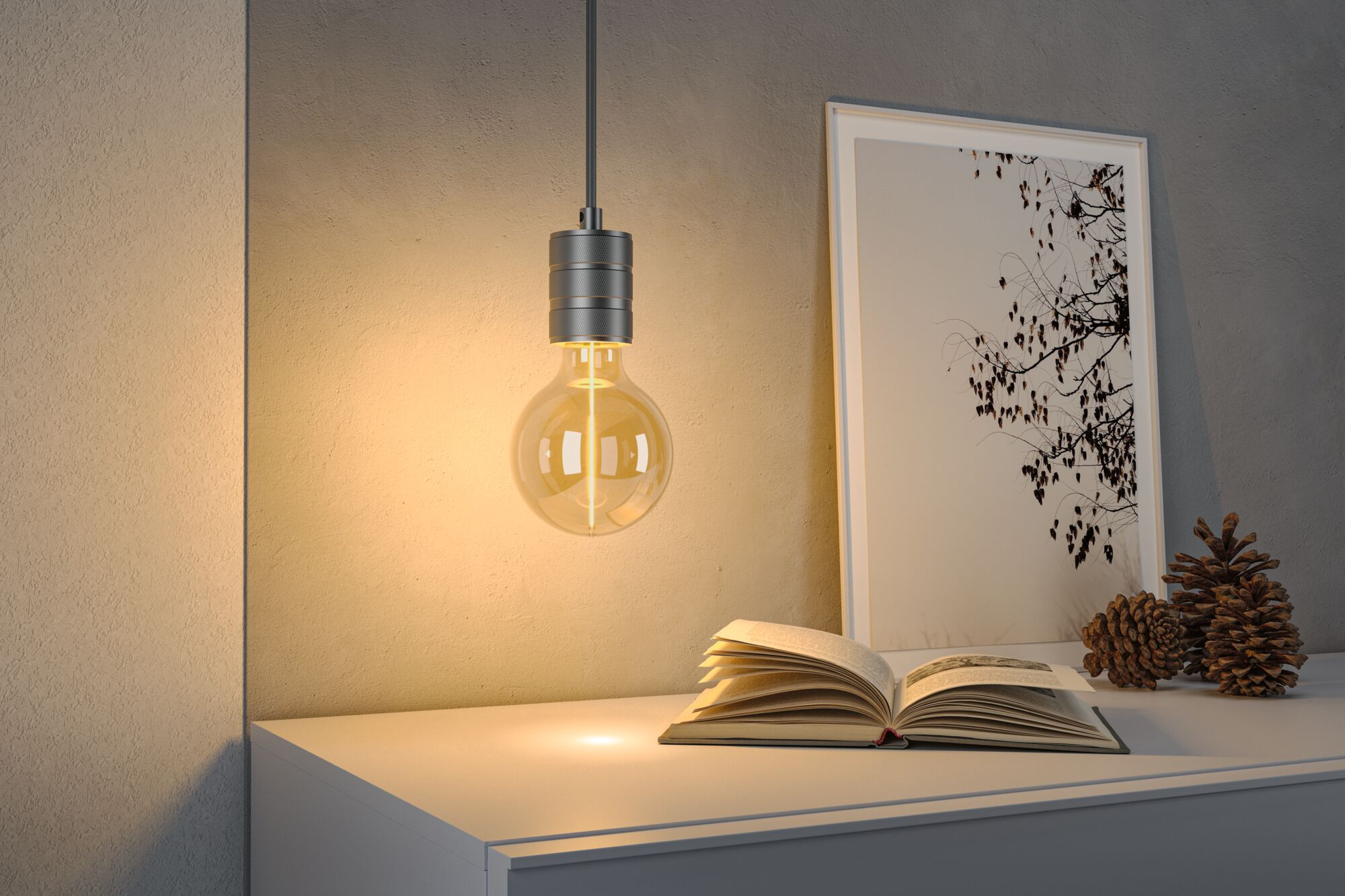 Świecąca żarówka nad otwartą książką na białej półce, obok obrazu i szyszek.