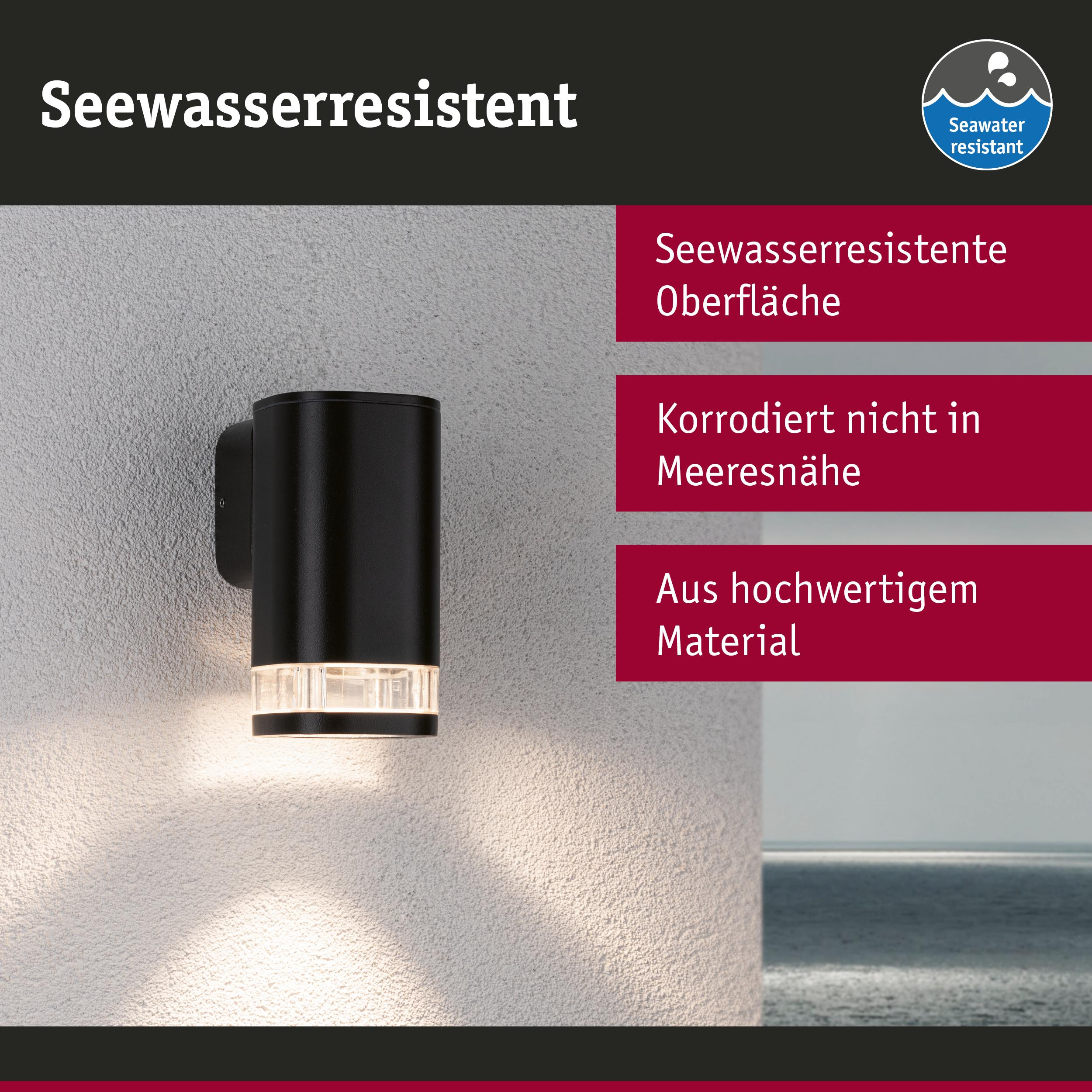 Schwarze Außenwandleuchte mit Glasdetail, Meer im Hintergrund.