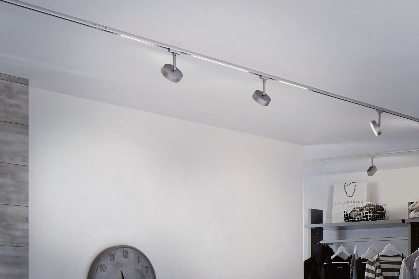Silberne Schienenlichter an einer Decke über Kleidung und einer Tasche.