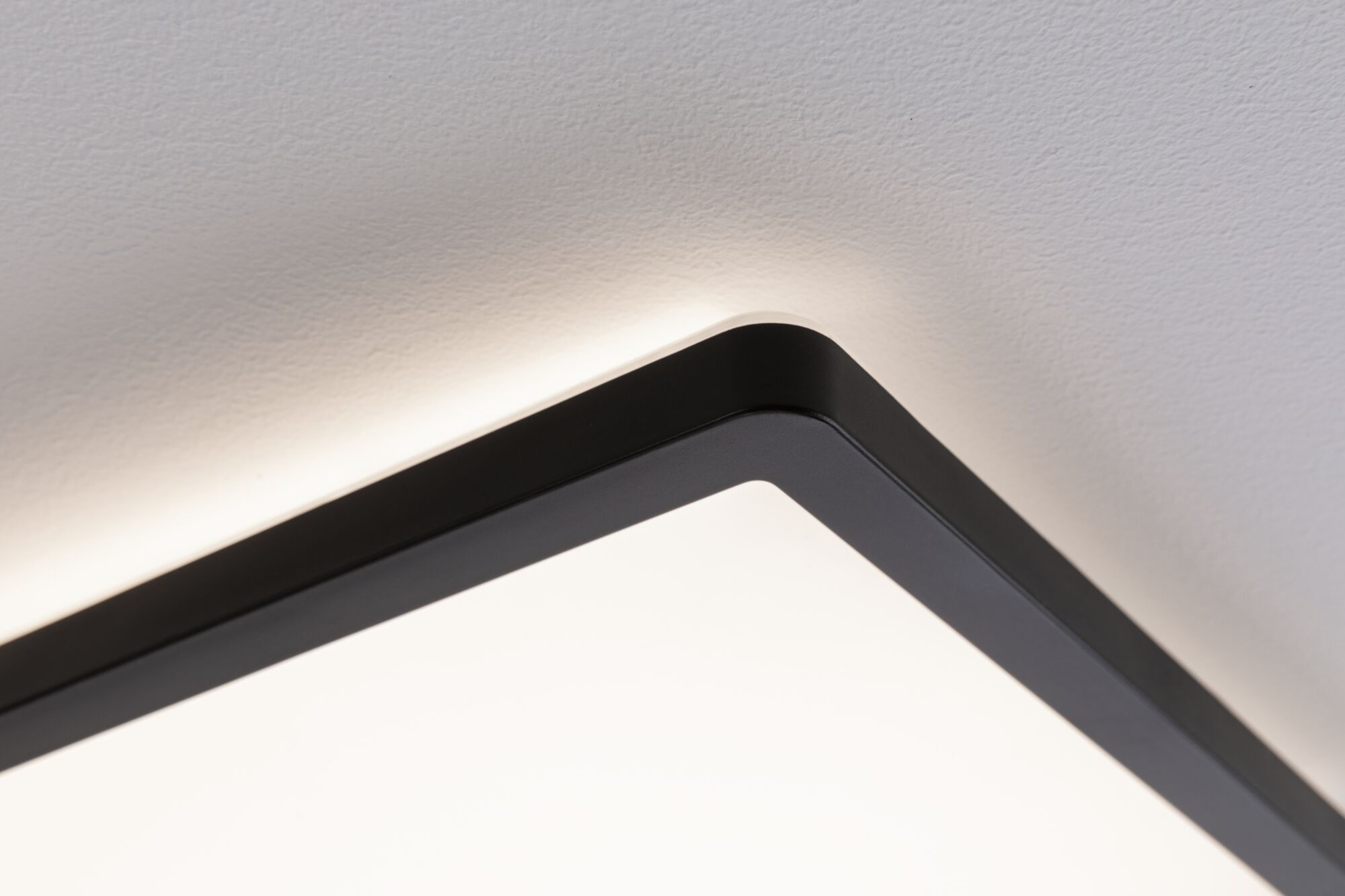 Primo piano di una lampada da soffitto nera con illuminazione indiretta su soffitto bianco.