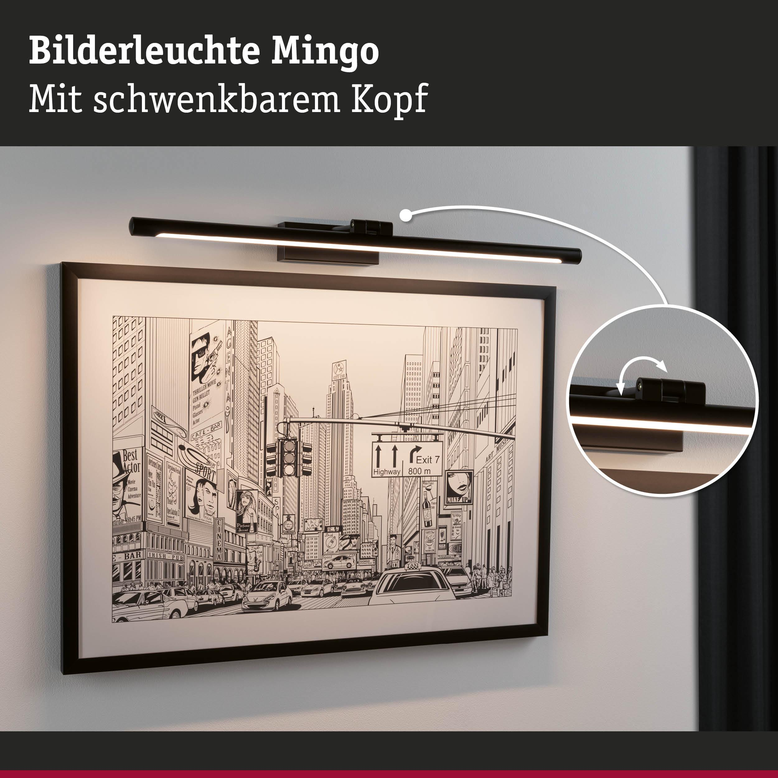 Ein schwarzer Bilderrahmen mit einer Stadtansicht, beleuchtet von einer Lampe.