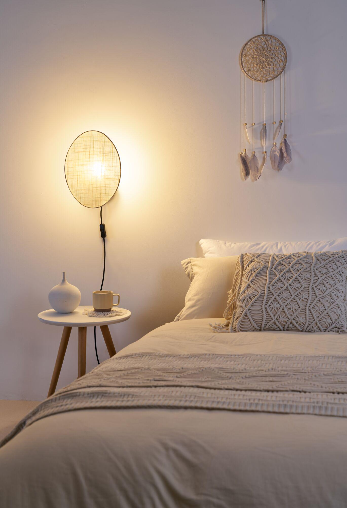 Stolik nocny z wazonem i kubkiem obok łóżka z poduszkami.