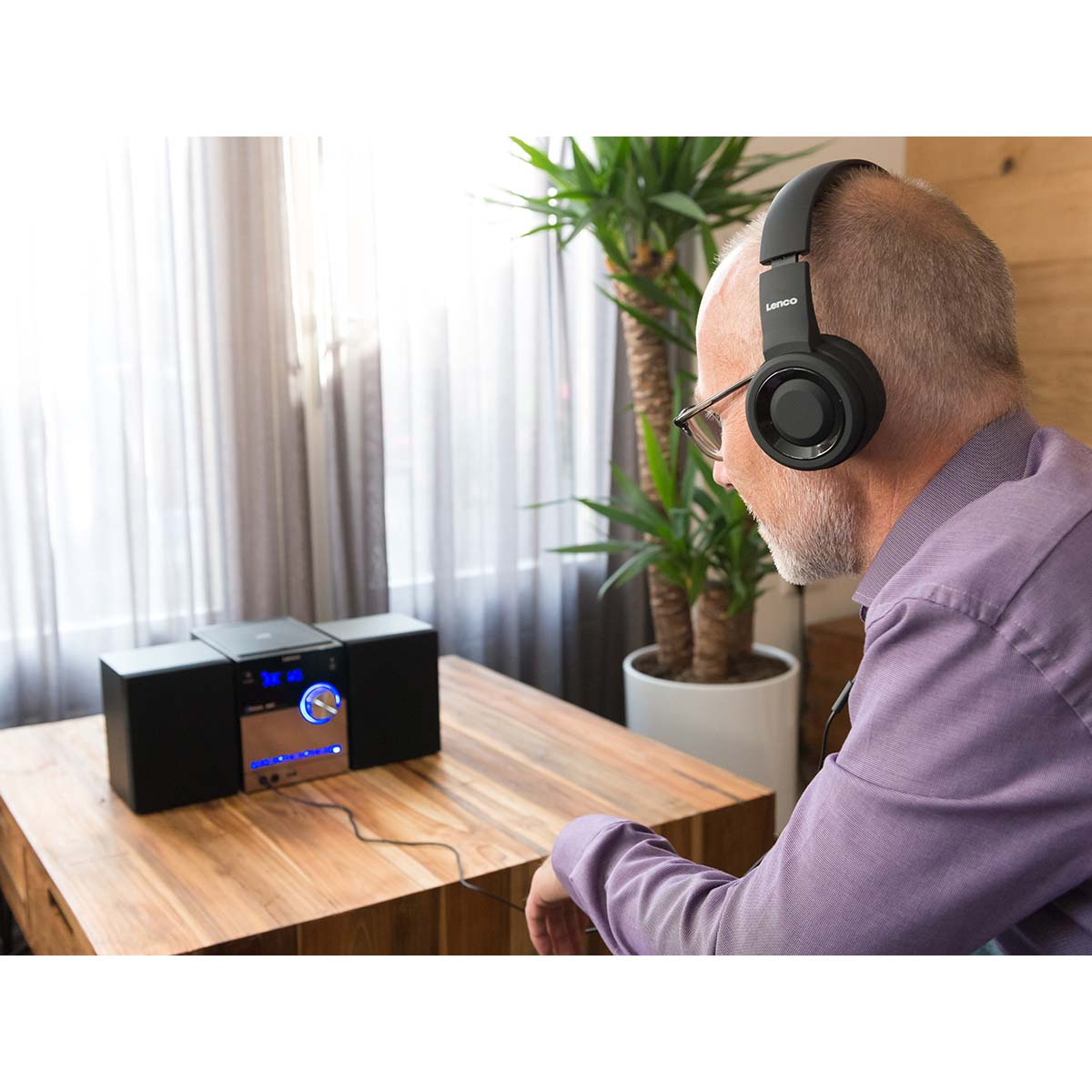 Mann mit Kopfhörern hört Musik von einer Stereoanlage auf einem Holztisch.