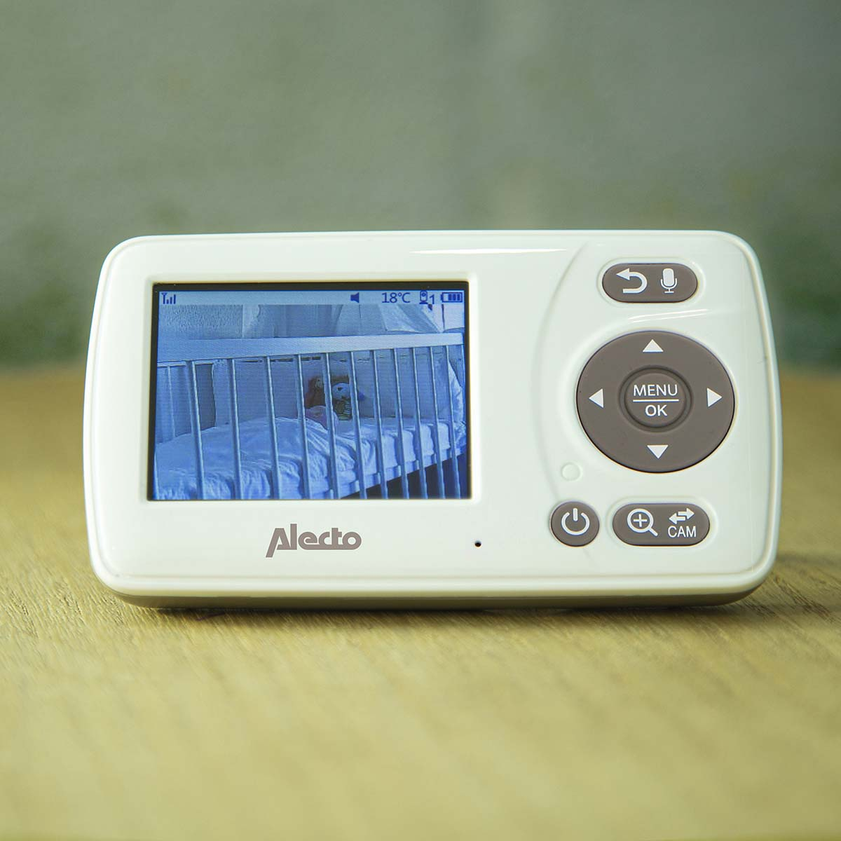 A white baby monitor showing a crib with a teddy bear. Temperature 18°C.