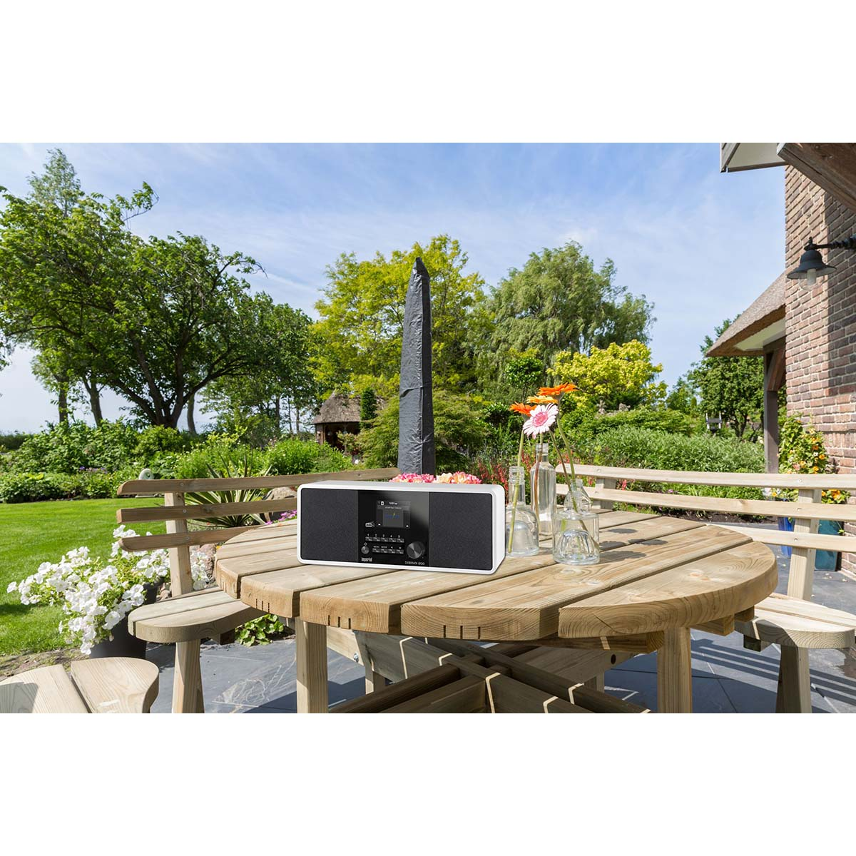 Białe radio na drewnianym stole ogrodowym z kwiatami i drzewami.