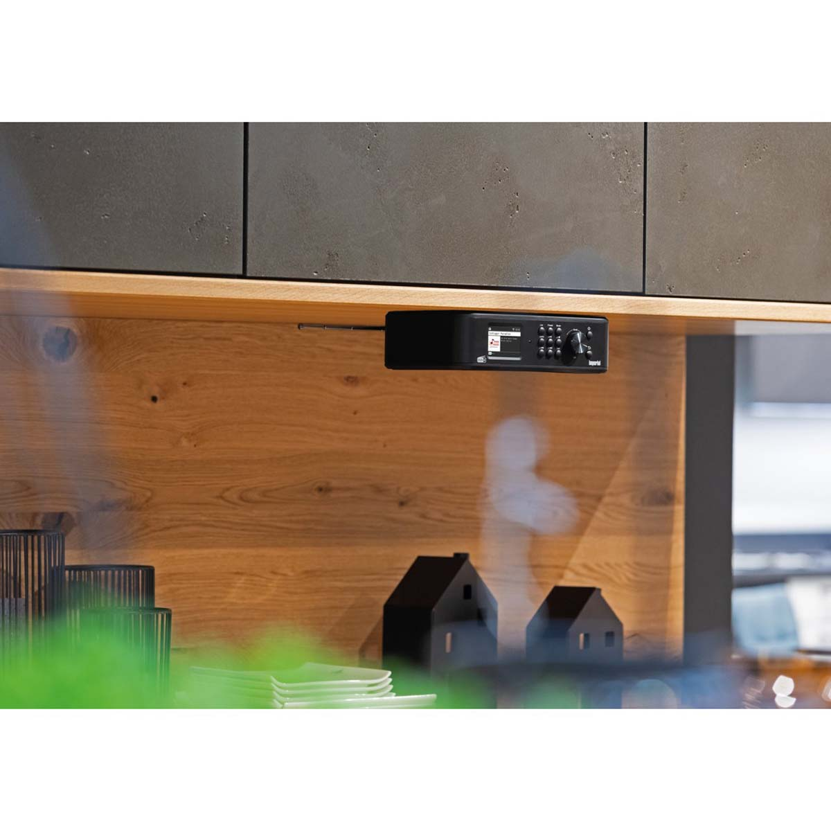 Czarno radio jest zamontowane pod drewnianą szafką. Dwie czarne figurki domków są poniżej.