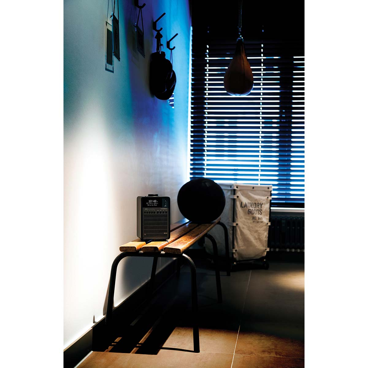 A black speaker and a ball on a wooden bench against a wall with hooks.
