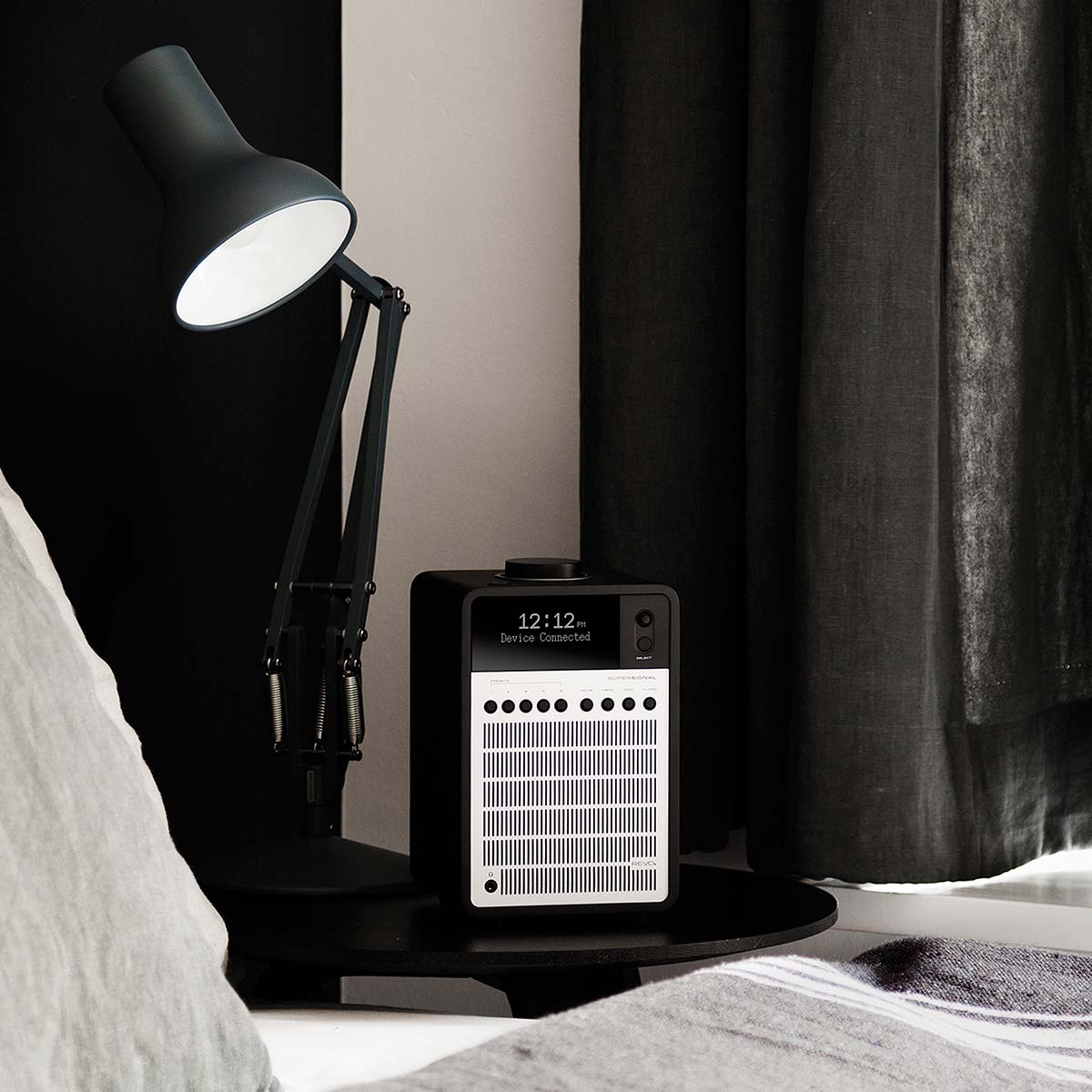 A black desk lamp arm extends over a black nightstand with a radio.