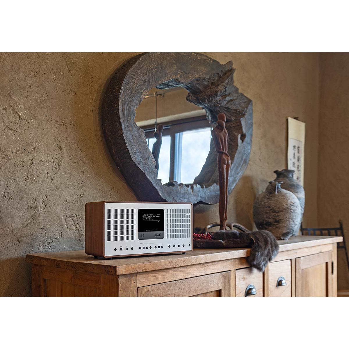 A wooden radio sits on a wooden dresser. A large, ornate mirror hangs on the wall behind it.