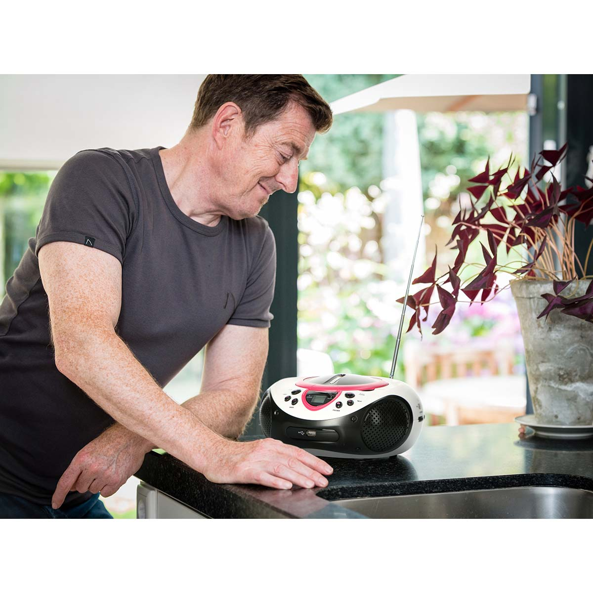 Un homme se penche sur un comptoir avec un lecteur CD et une plante.