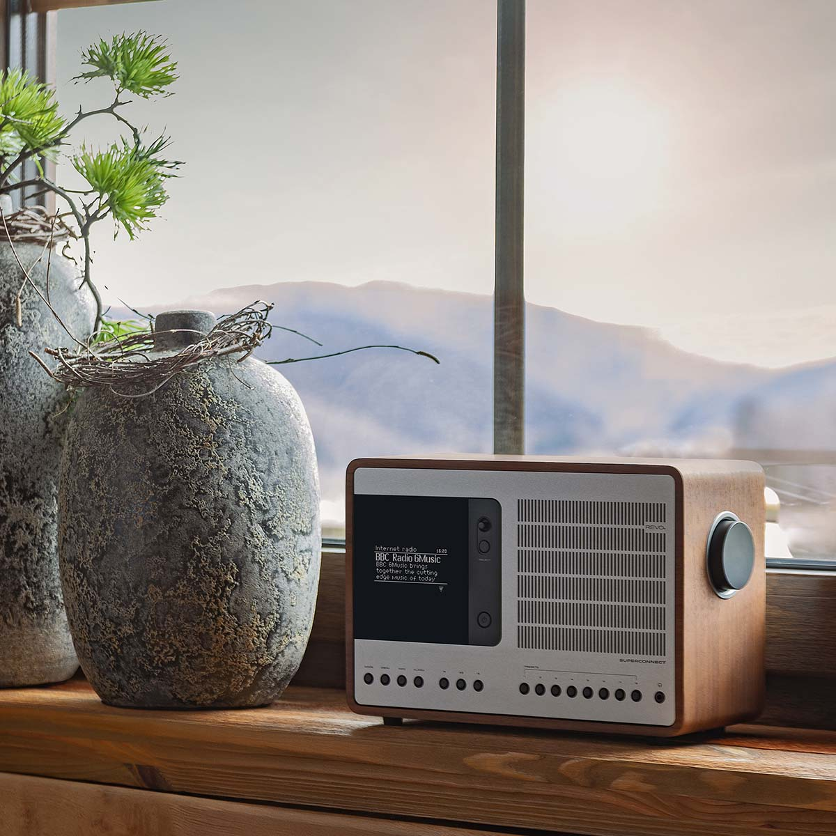 Ein Holzradio mit Display steht auf einem Fensterbrett mit Blick auf Berge.